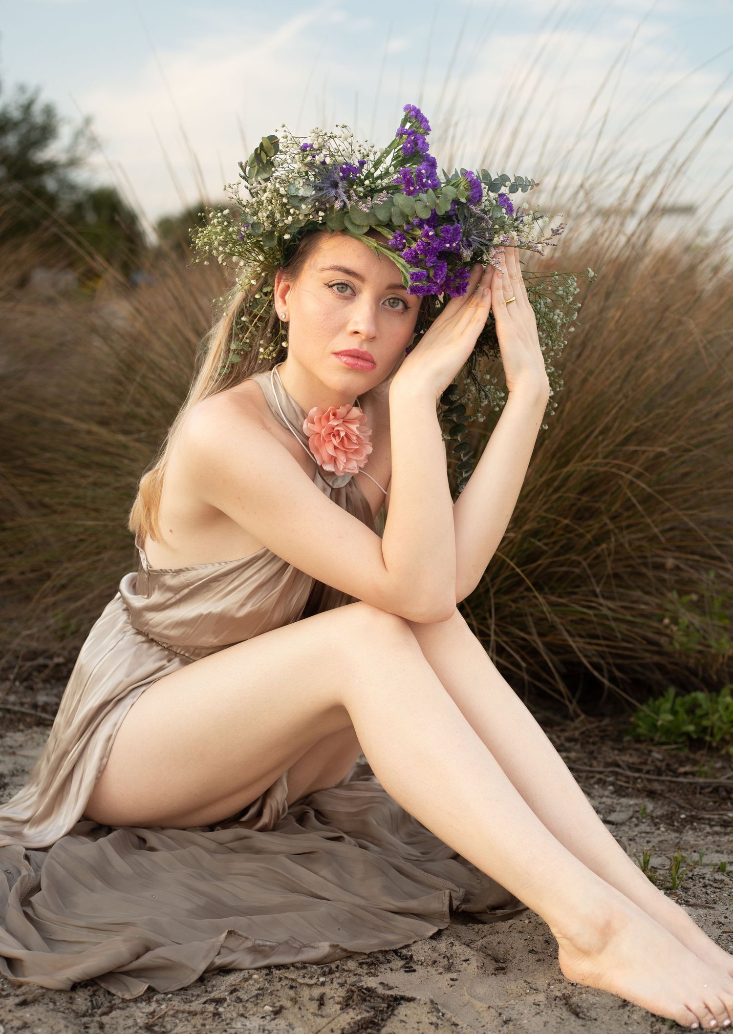 Bohemian style portrait with floral crown and neutral dress on sandy beach.