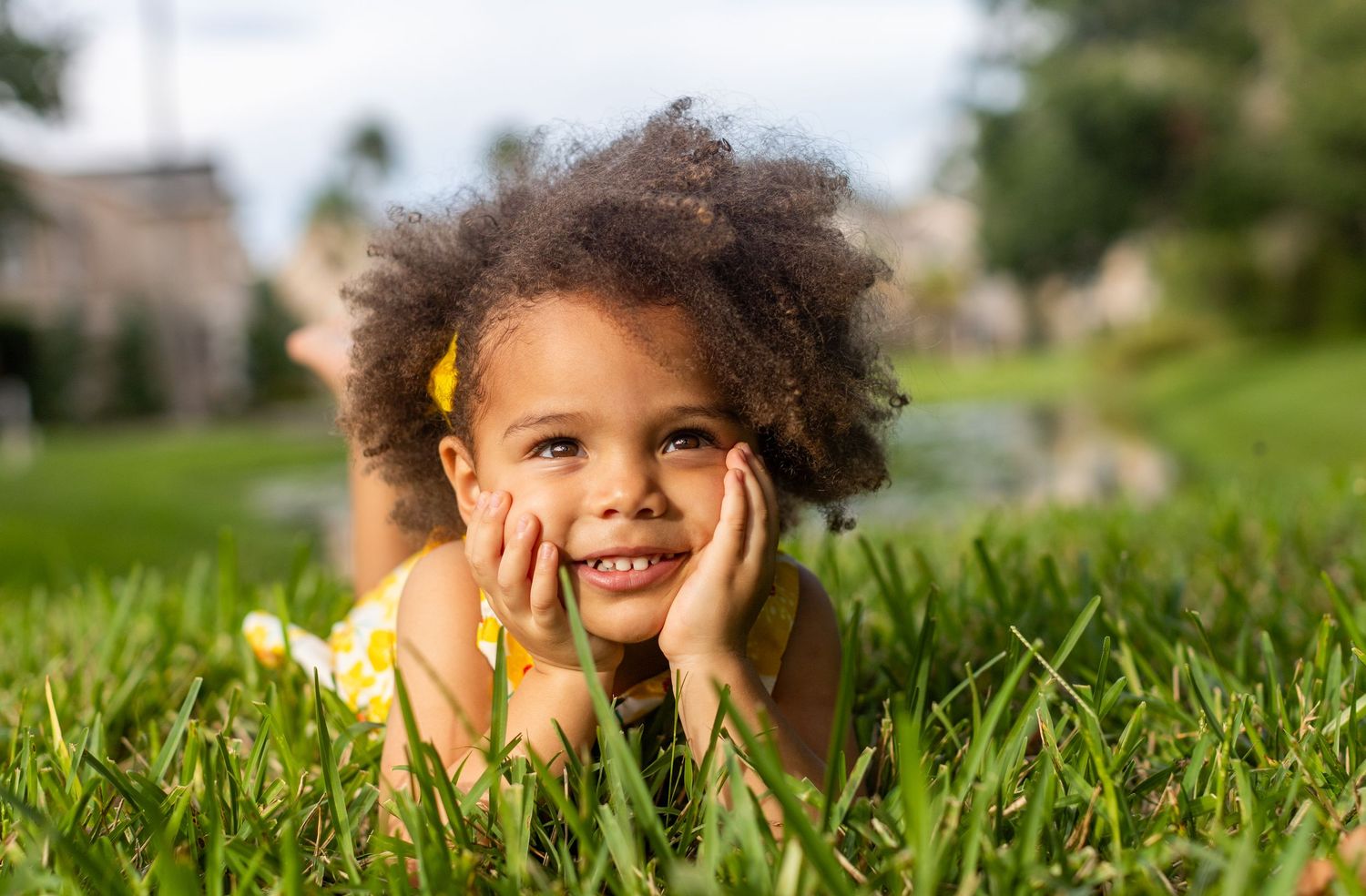 Smiling child lying in lush green grass during outdoor photo session.