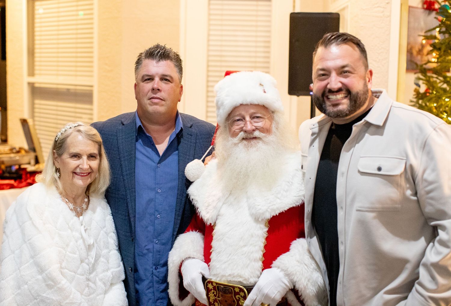 Group poses for a festive holiday photo with Santa Claus in front of a decorated tree.