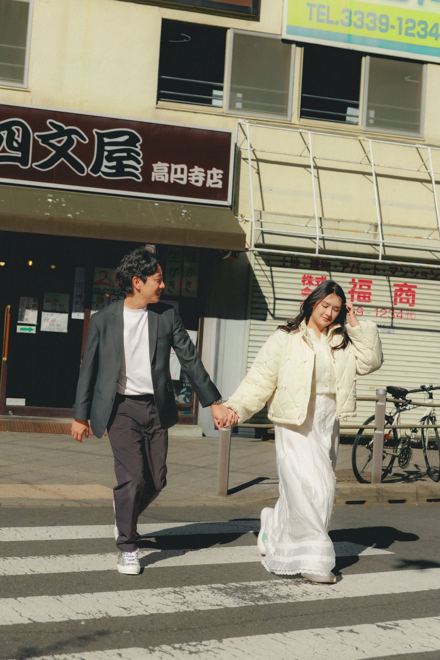 Two people dance playfully on a sidewalk outside a storefront in a candid sequence of motion in Japan.
