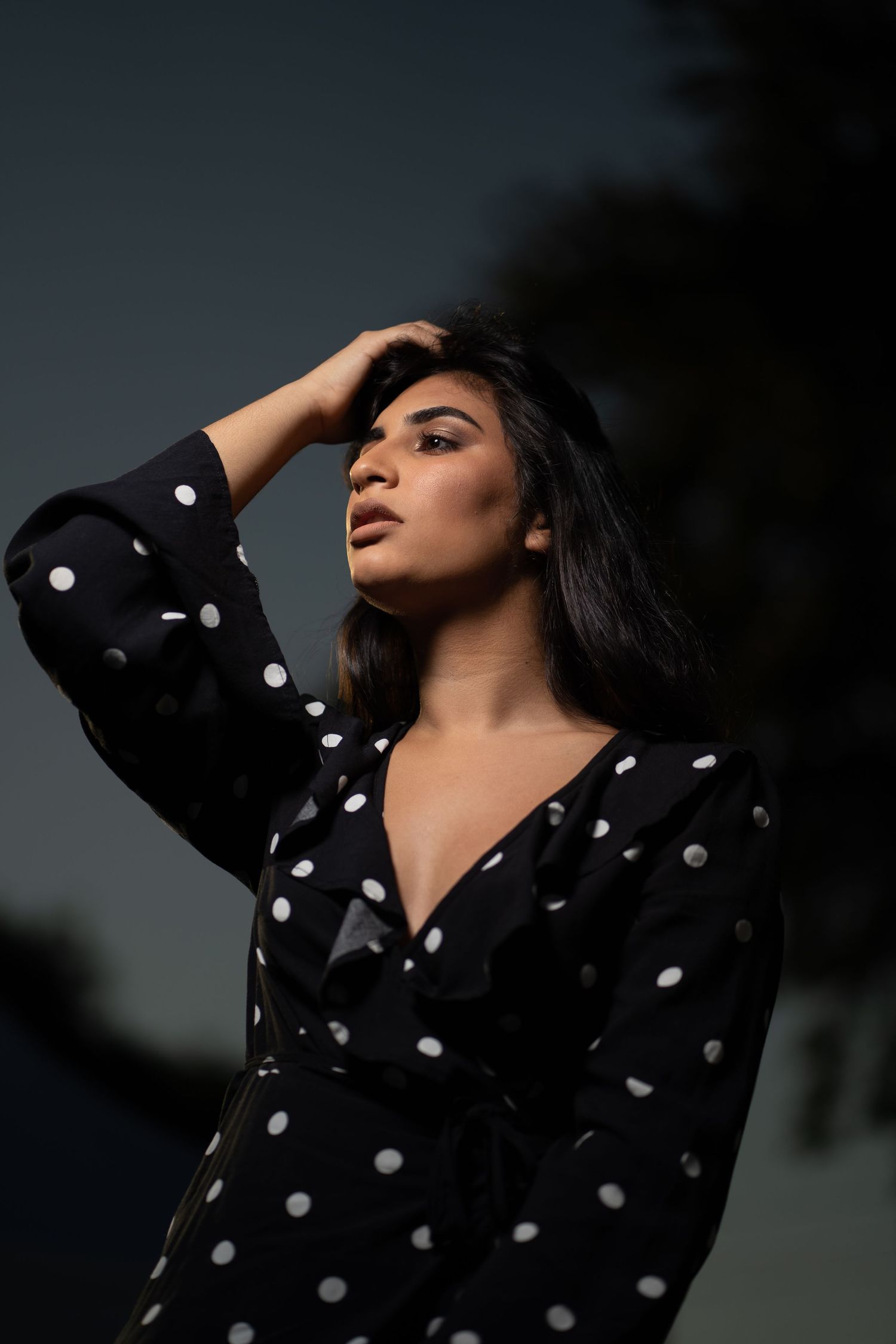 Woman brushing her hair back while wearing a polka-dot blouse.