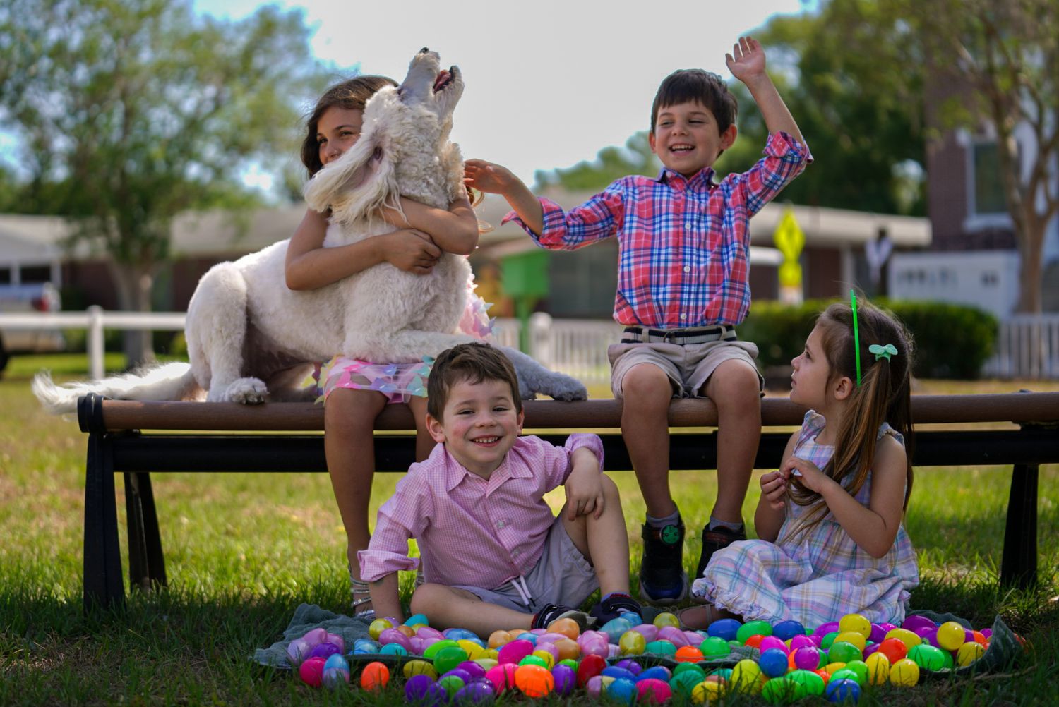 Children sitting on a bench surrounded by colorful Easter eggs with a family pet.