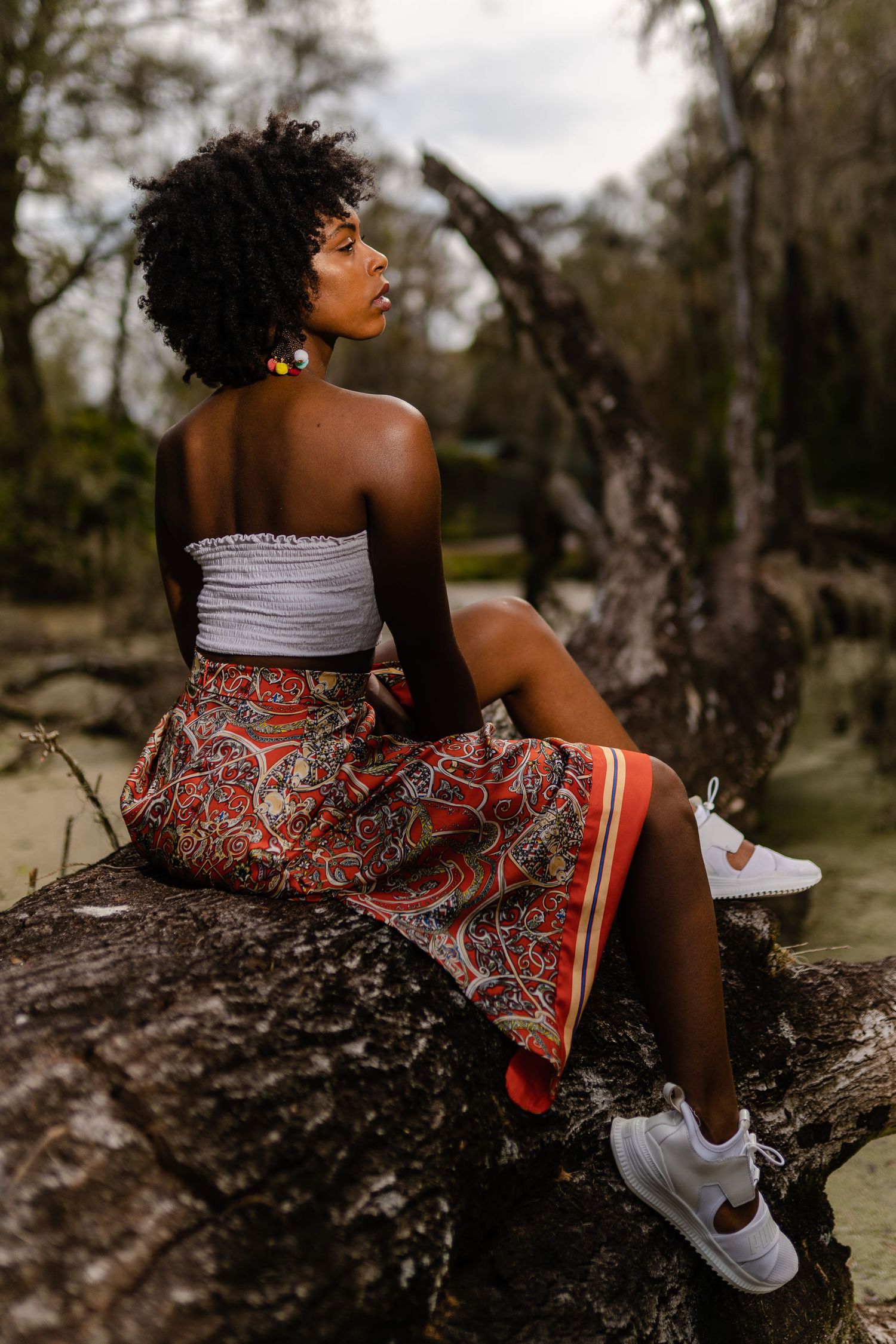 Woman sitting on a large tree trunk outdoors in patterned dress.
