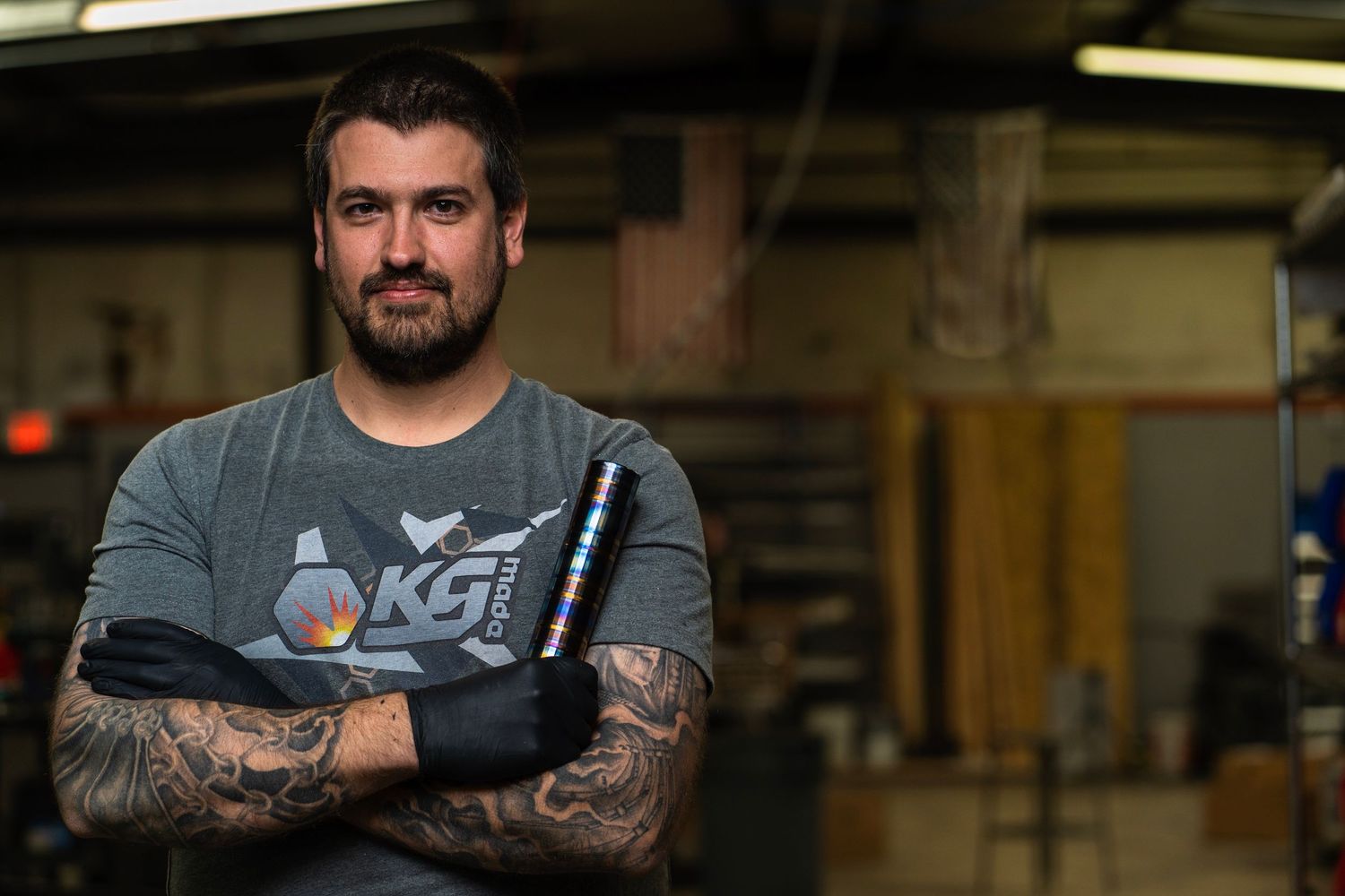 Man with tattoos crossing his arms in a workshop setting.