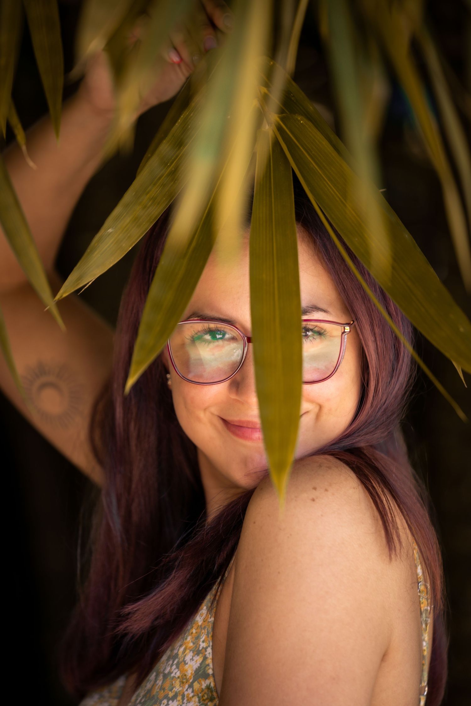Woman smiling playfully while peeking through palm leaves.