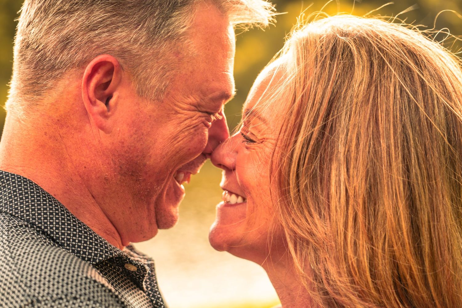 Older couple smiling nose-to-nose in a golden sunset.