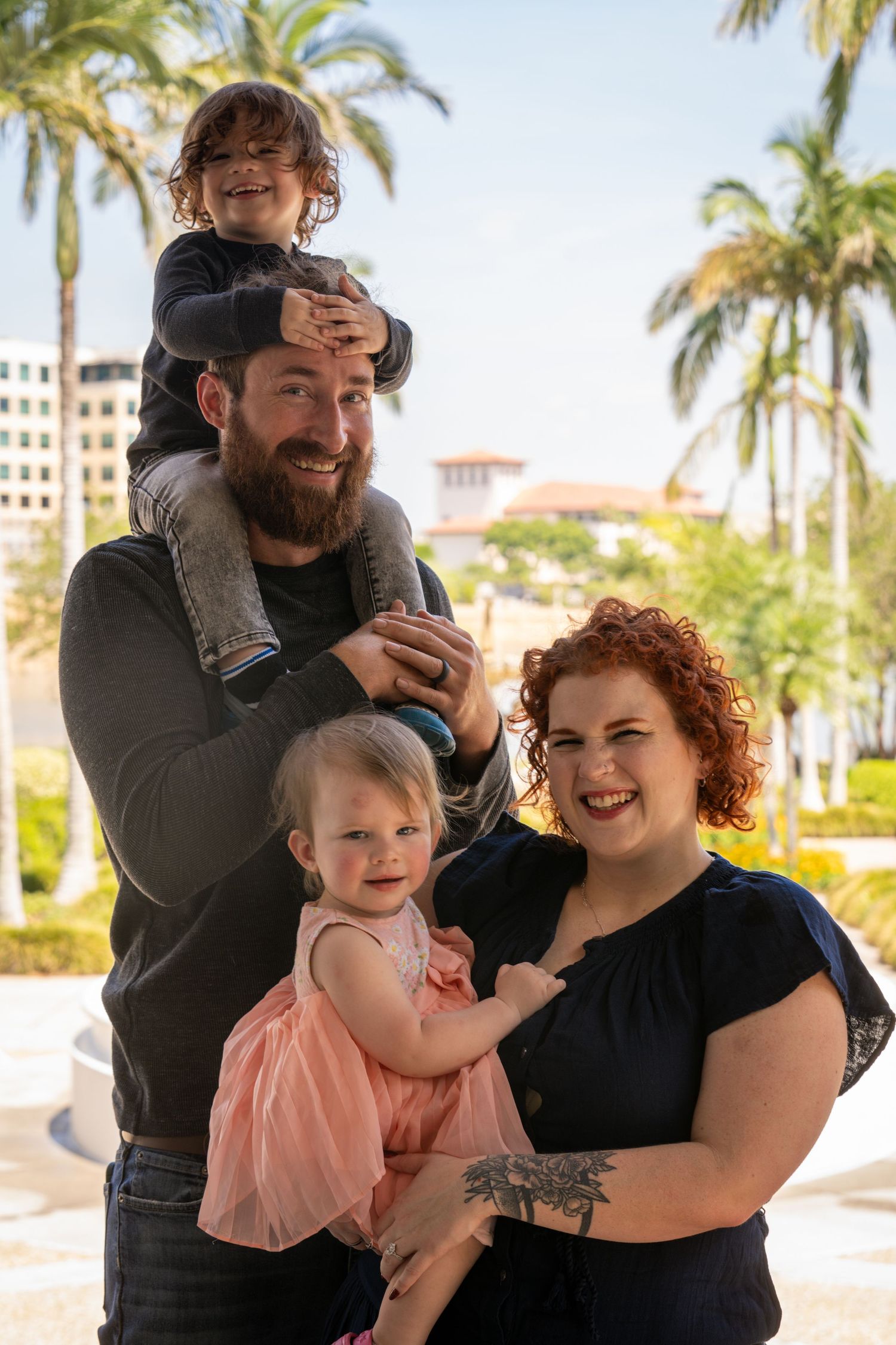 Family of three posing together outdoors with palm trees in the background.