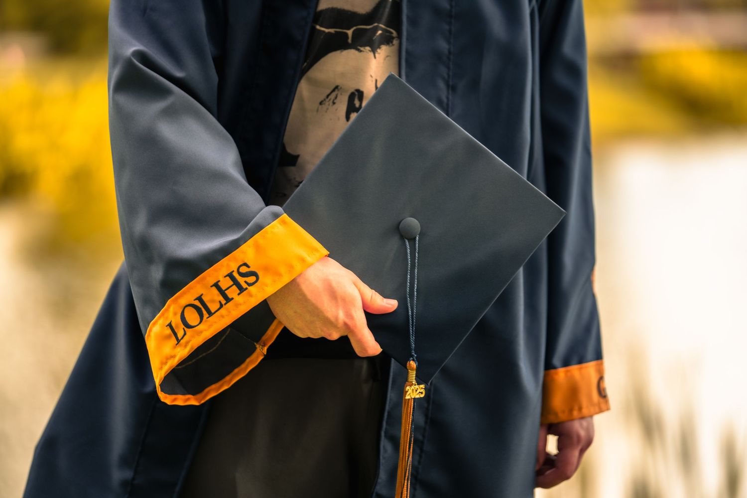 Close-up of a graduate holding cap and gown with golden tassel details.