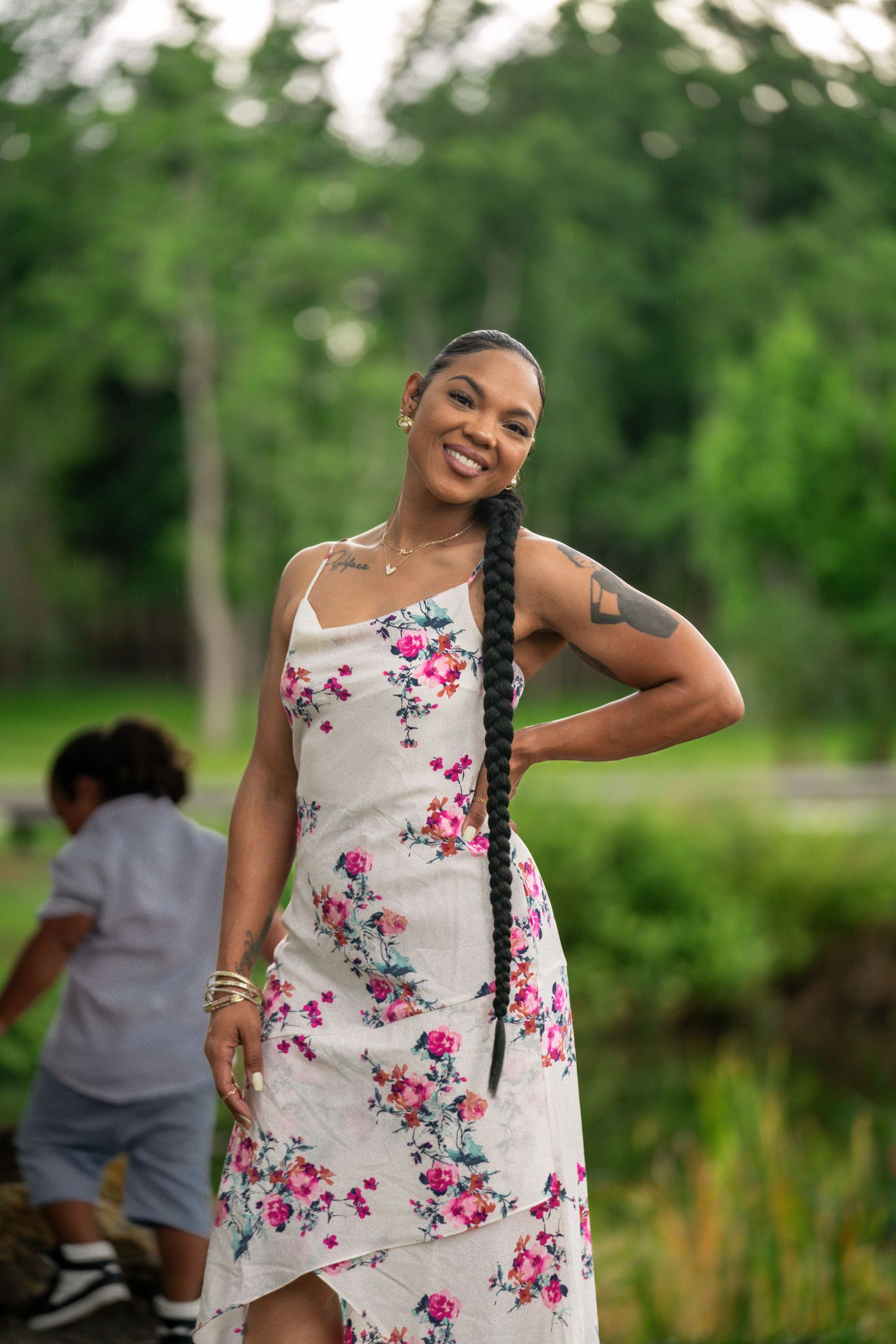 Young woman in floral dress posing playfully with a son in the background.