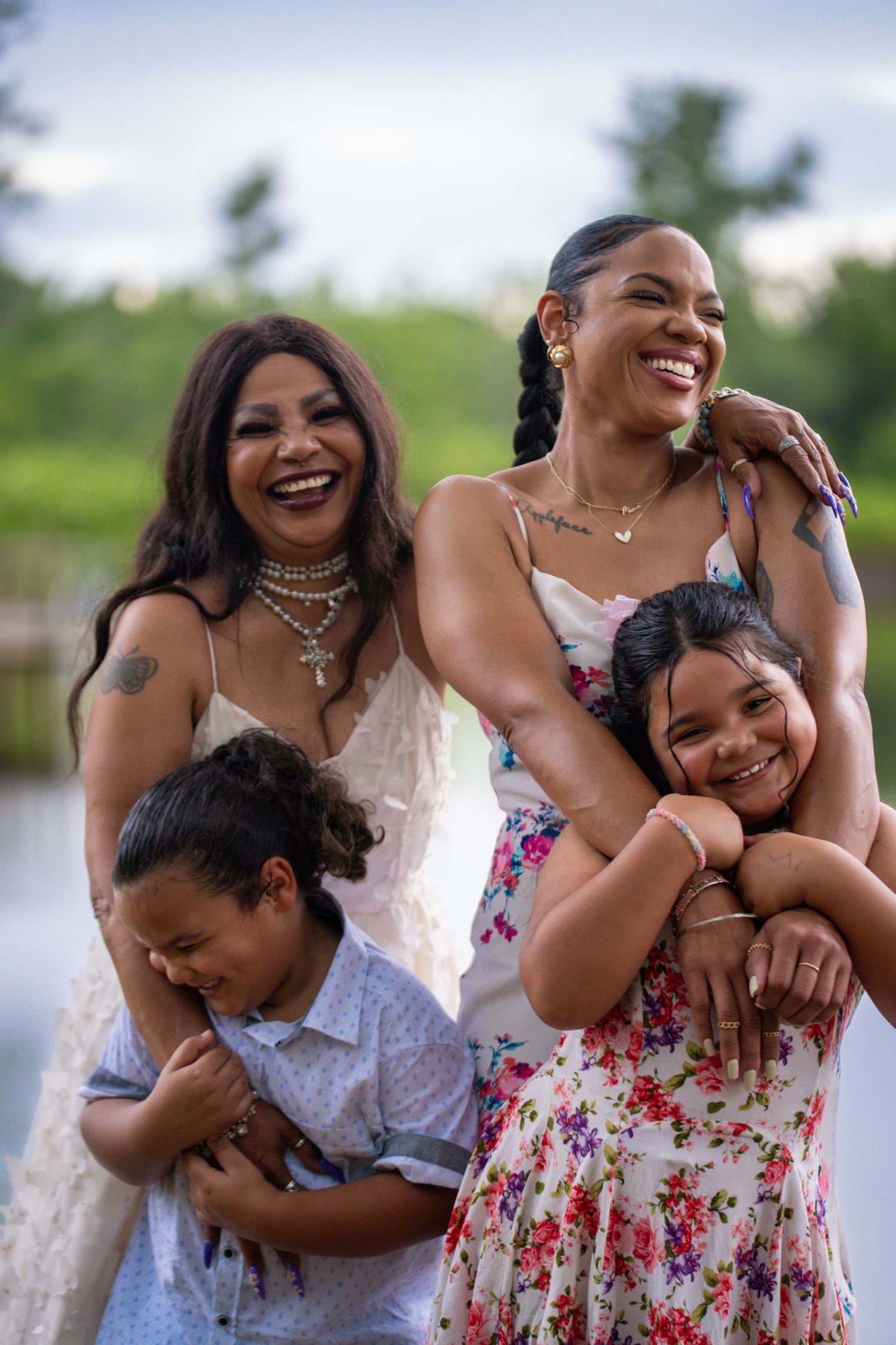 Mother in a floral dress holding two children while standing with two more smiling kids.