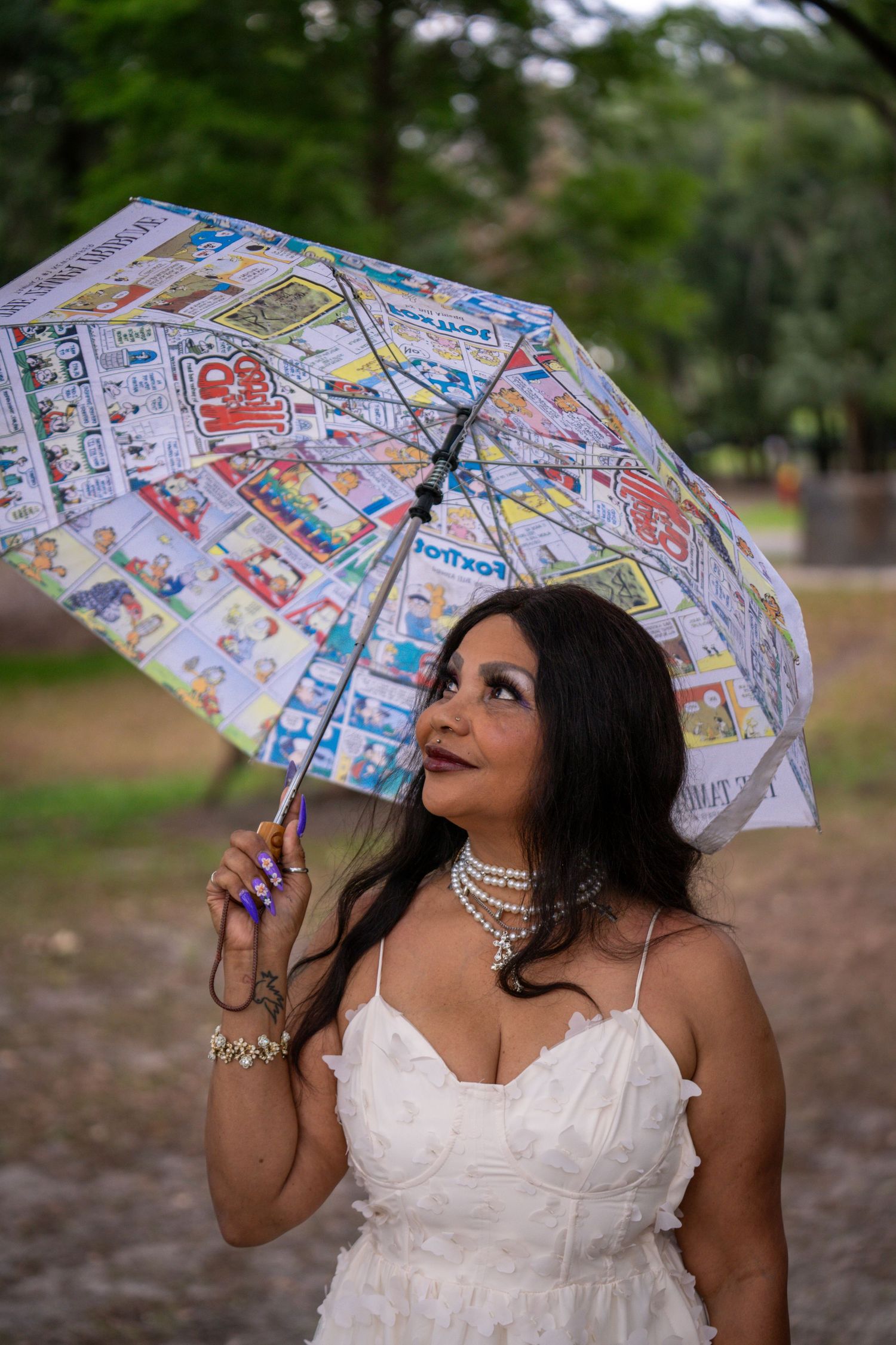 Bride in a white gown holding a colorful umbrella in the rain.