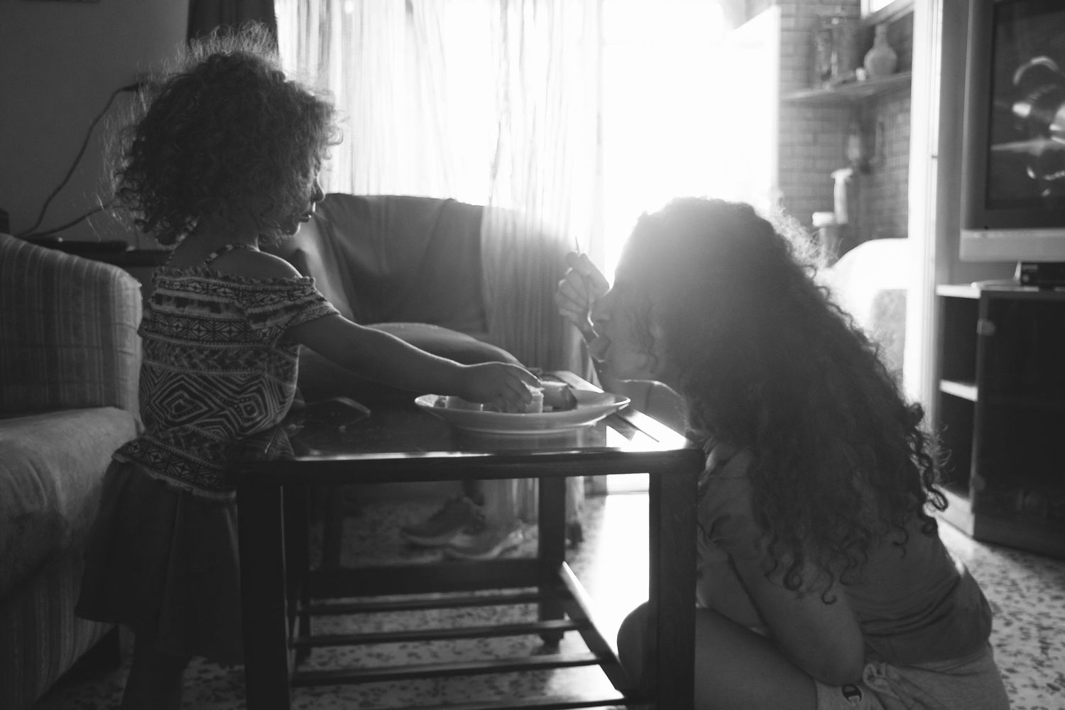 Black and white picture of mother and daughter eating together with similar frizzy hair during a chilled photo session at home  in Ottawa