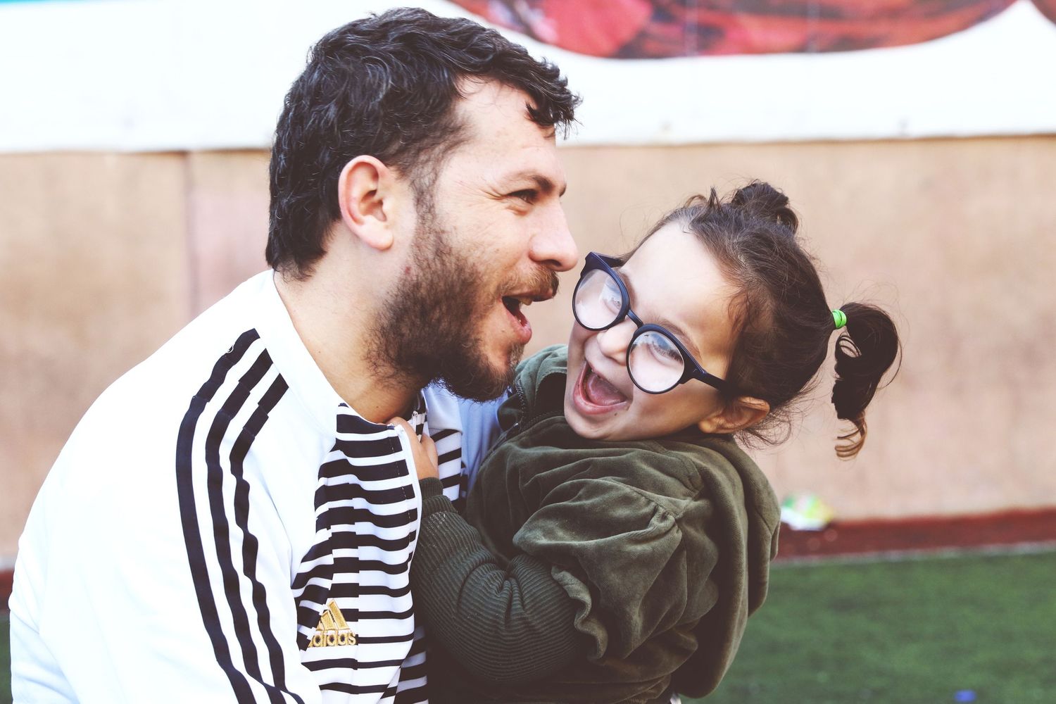father and daughter together playfully smiling while he is holding her during a relaxed outdoor family photography session