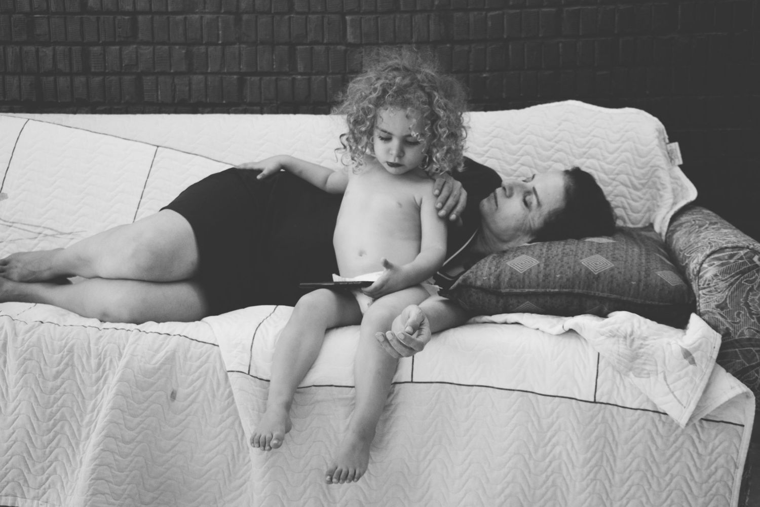 Black and white photo of a child sitting on a bed with her mother lying behind her during an at-home family photography session  in Ottawa