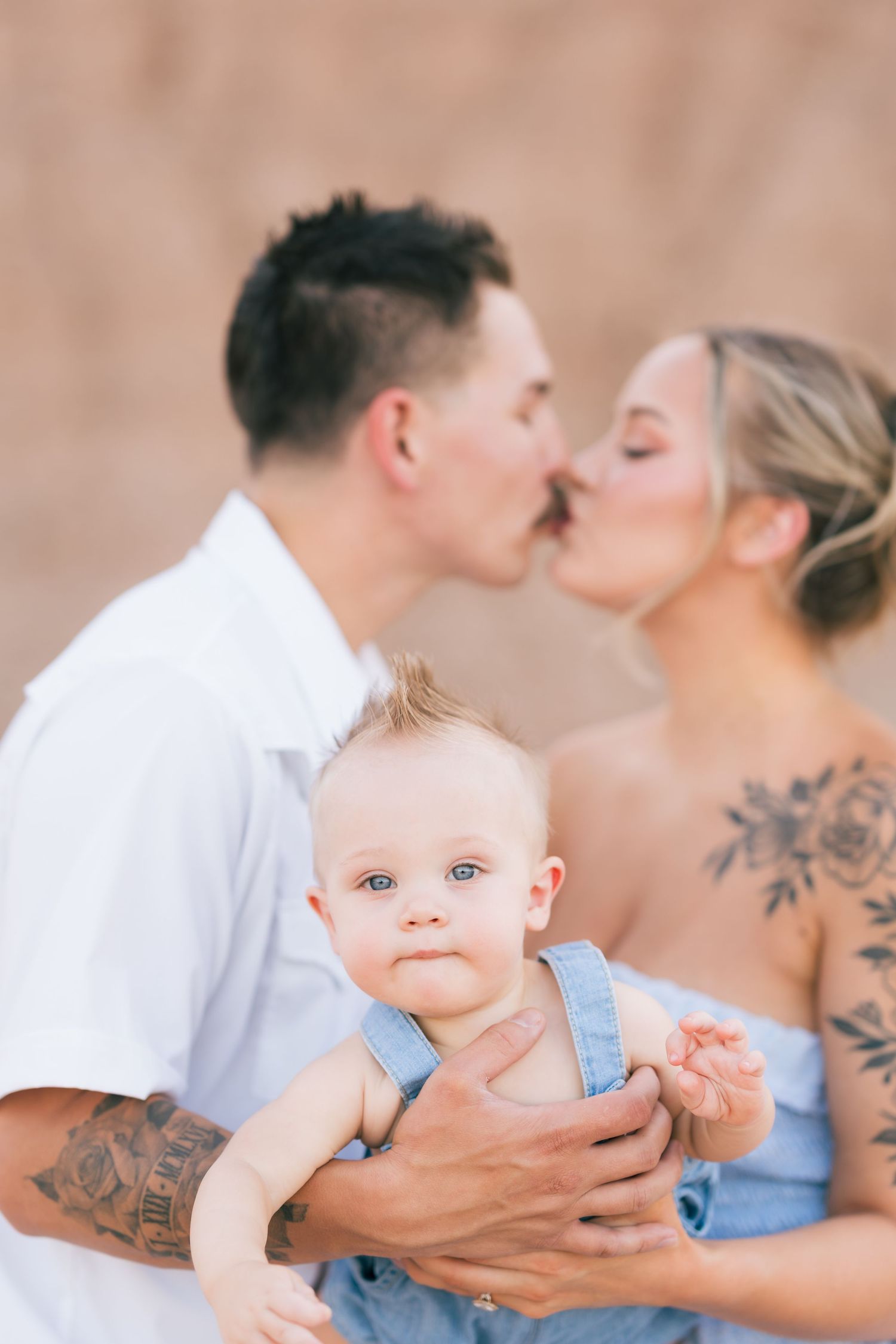 Parents kissing while holding their child during a family portrait session at Red Knolls, Arizona.