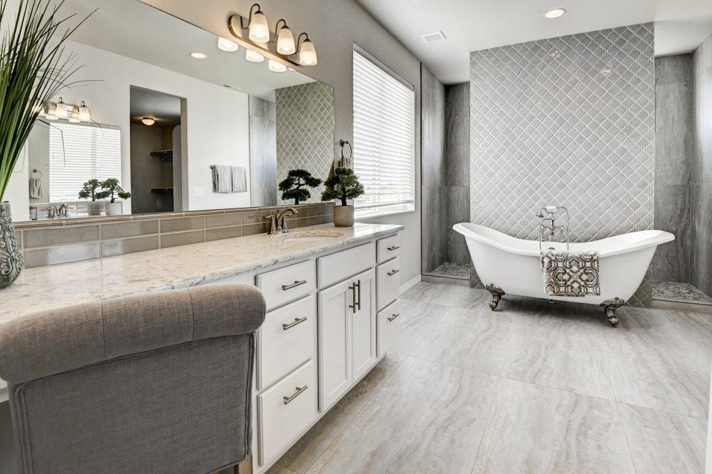 Luxurious gray bathroom with freestanding clawfoot tub, double vanity, and decorative tile accent wall.