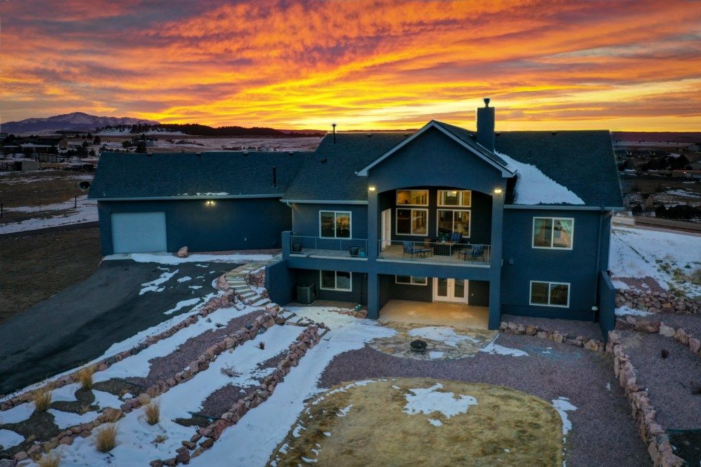 Stunning aerial view of large two-story blue home at sunset with snow-dusted landscape and mountain views.