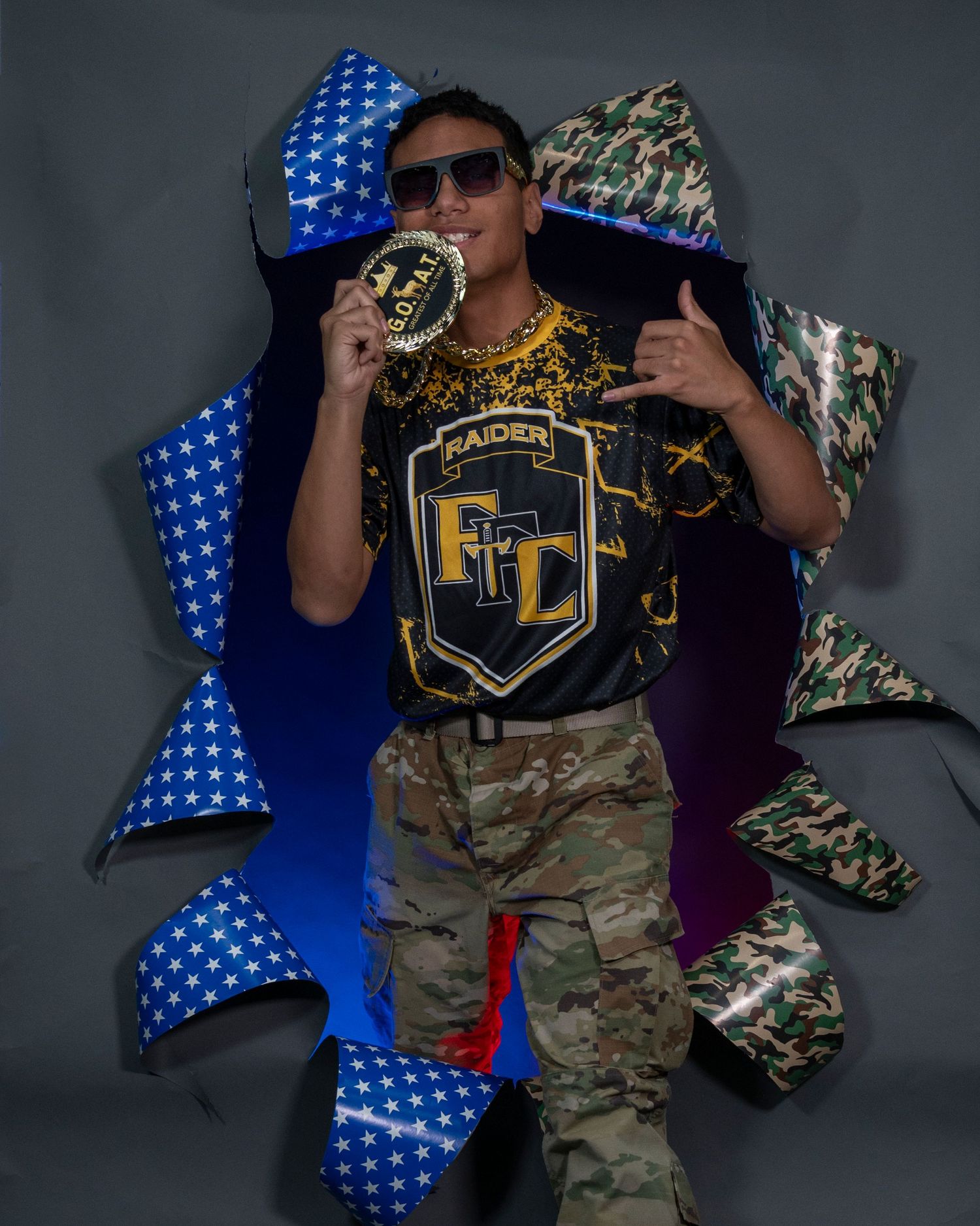 Student in Raiders JROTC uniform posing dramatically with camo and star-patterned background.