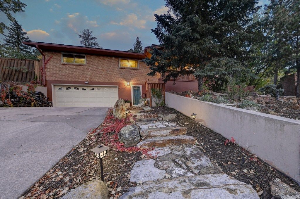Brick ranch-style home with attached garage, stone steps, and mature trees at twilight.