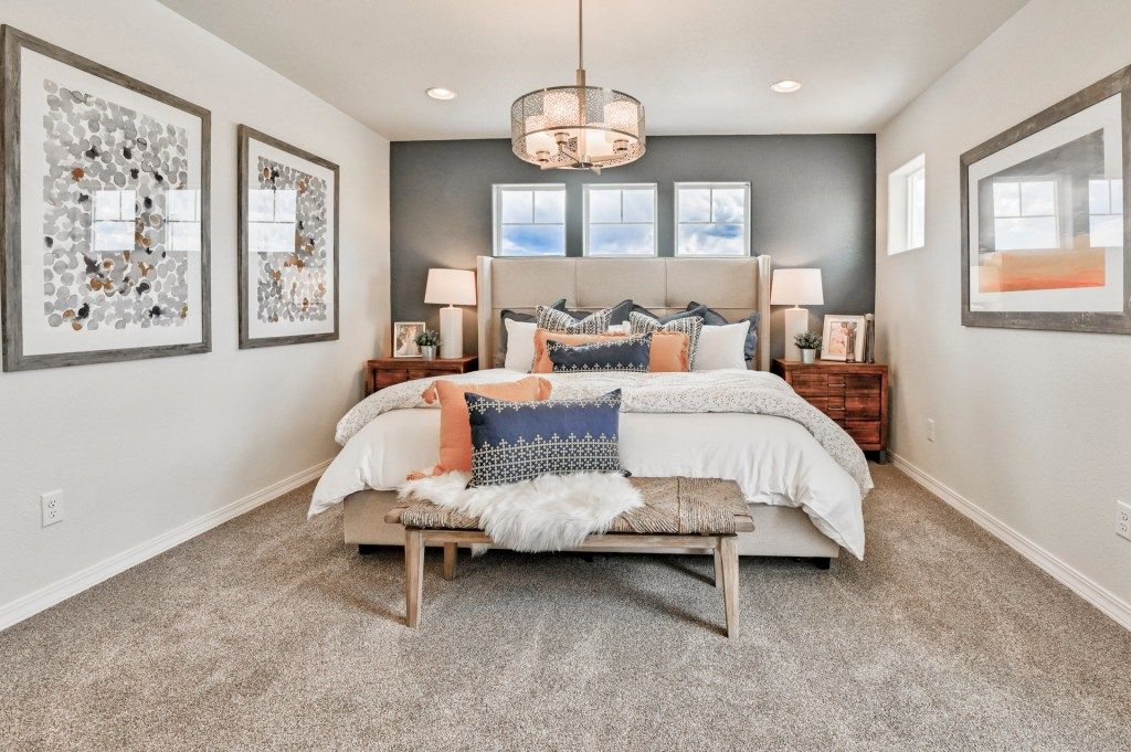 Elegant master bedroom with gray accent wall, chandelier, neutral carpet, and coordinated bedding with orange accents.