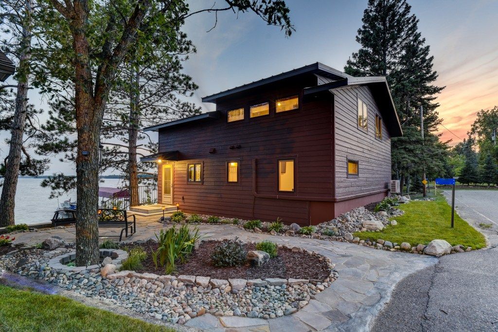 Rustic wood-sided two-story home at sunset surrounded by tall pine trees with landscaped rock garden.