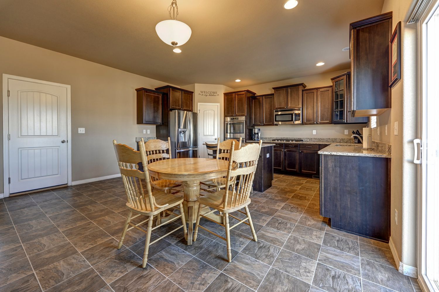 Elegant kitchen and dining area with dark wood cabinets, granite counters, stainless appliances, and tile flooring.