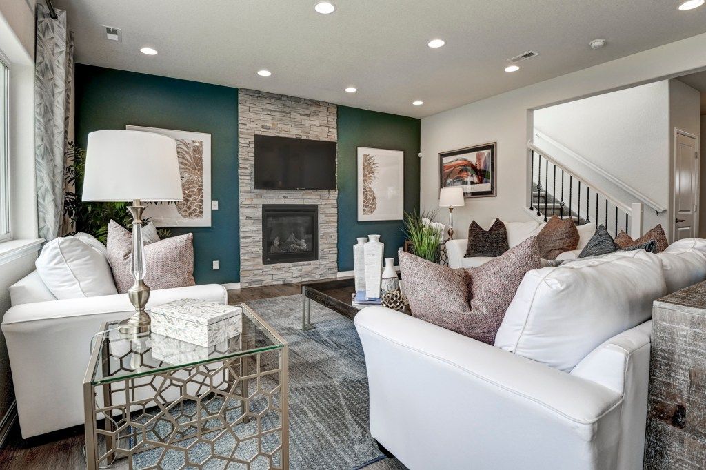 Modern living room with teal accent wall, stone fireplace, white sofas, recessed lighting, and staircase.