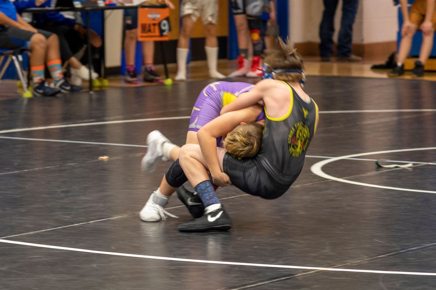 Two youth wrestlers competing on a blue mat during an indoor wrestling tournament.