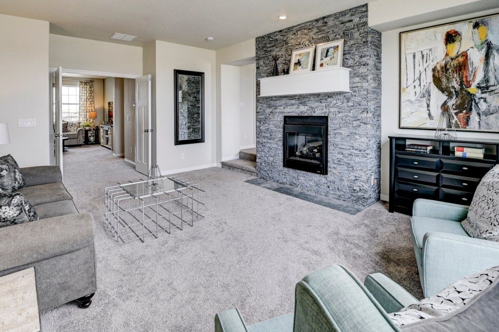 Modern living room with stone fireplace, neutral carpet, gray sectional sofa, and contemporary artwork.