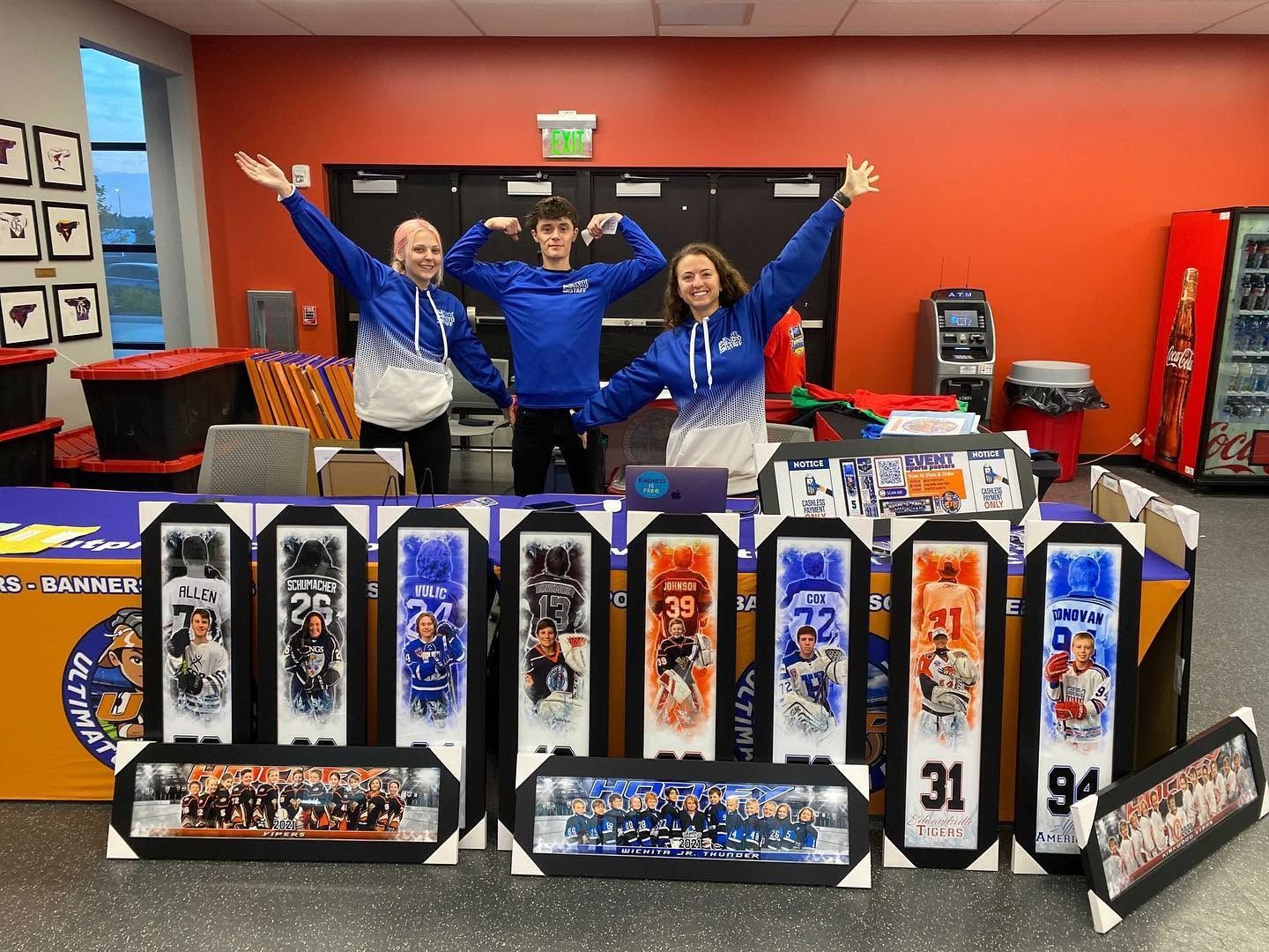 Three people posing with framed sports banners and memorabilia displays in a team store.