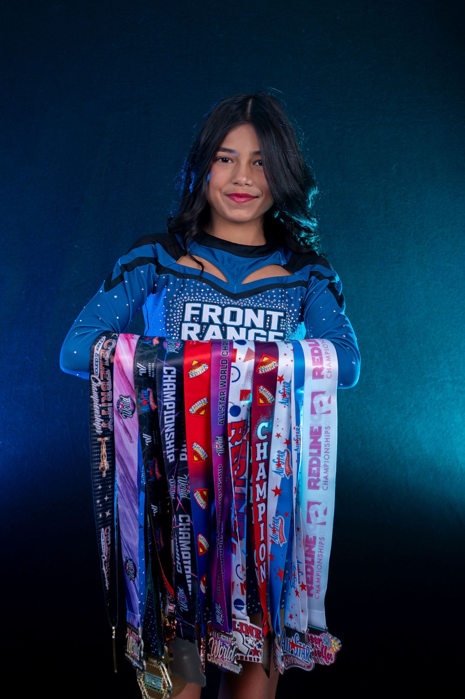 Young girl in blue Front Range cheer uniform proudly displaying a collection of championship medals.
