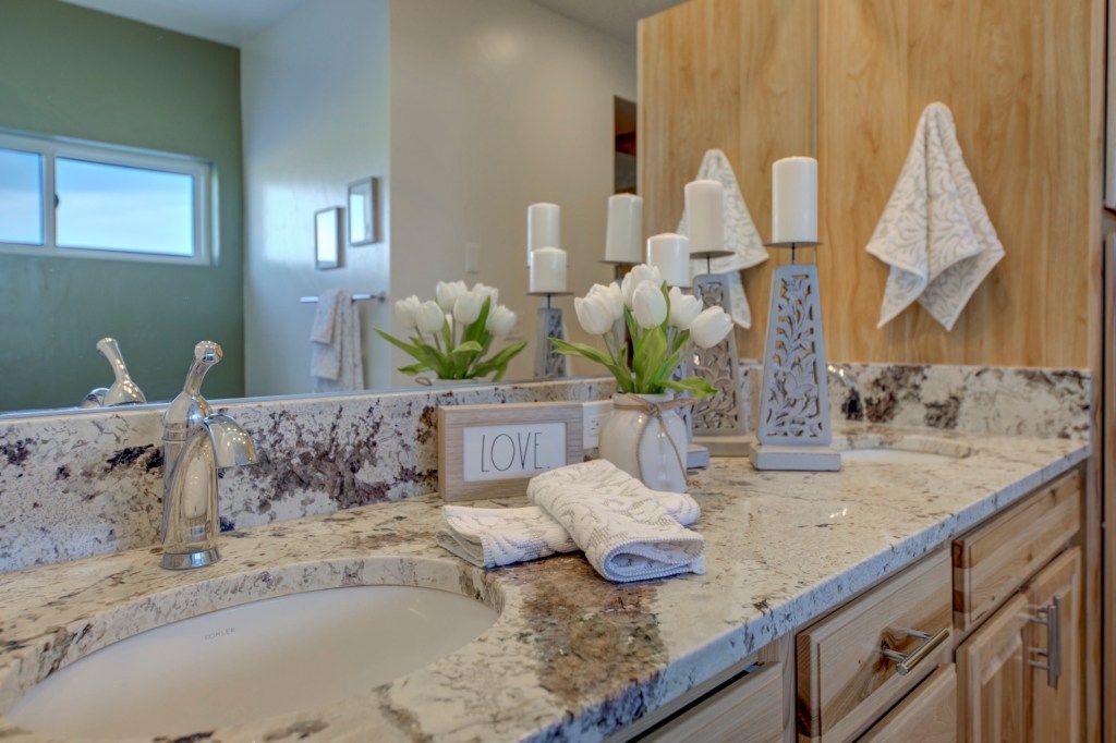 Elegant bathroom vanity with granite countertop, undermount sink, wood cabinets, and decorative white floral accents.