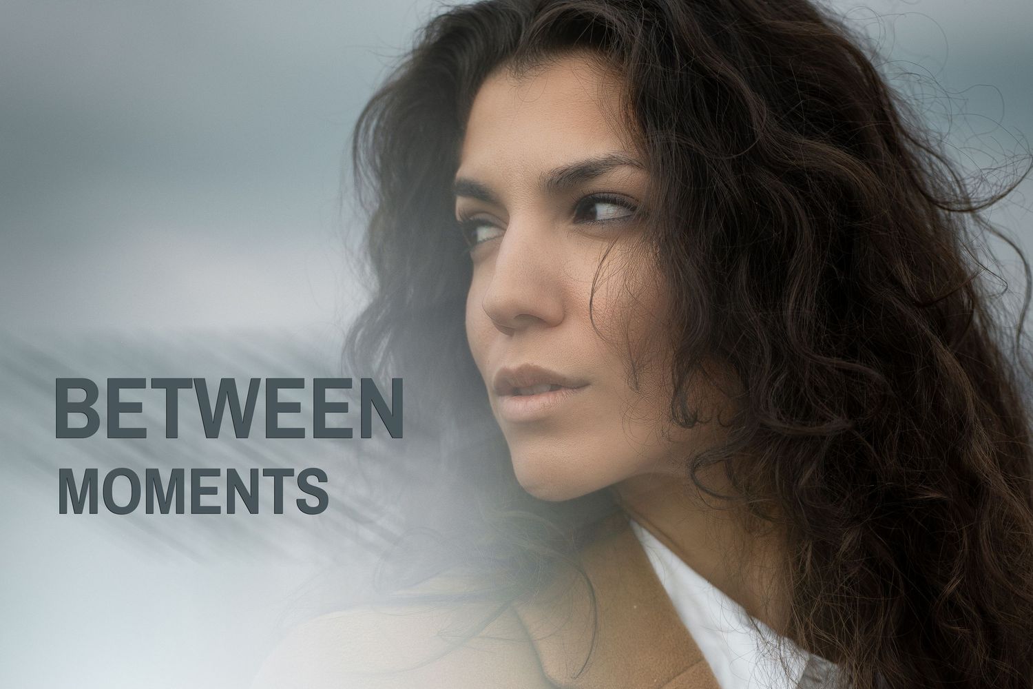 A pensive young woman with curly dark hair gazes into the distance, overlaid with the text Between Moments.