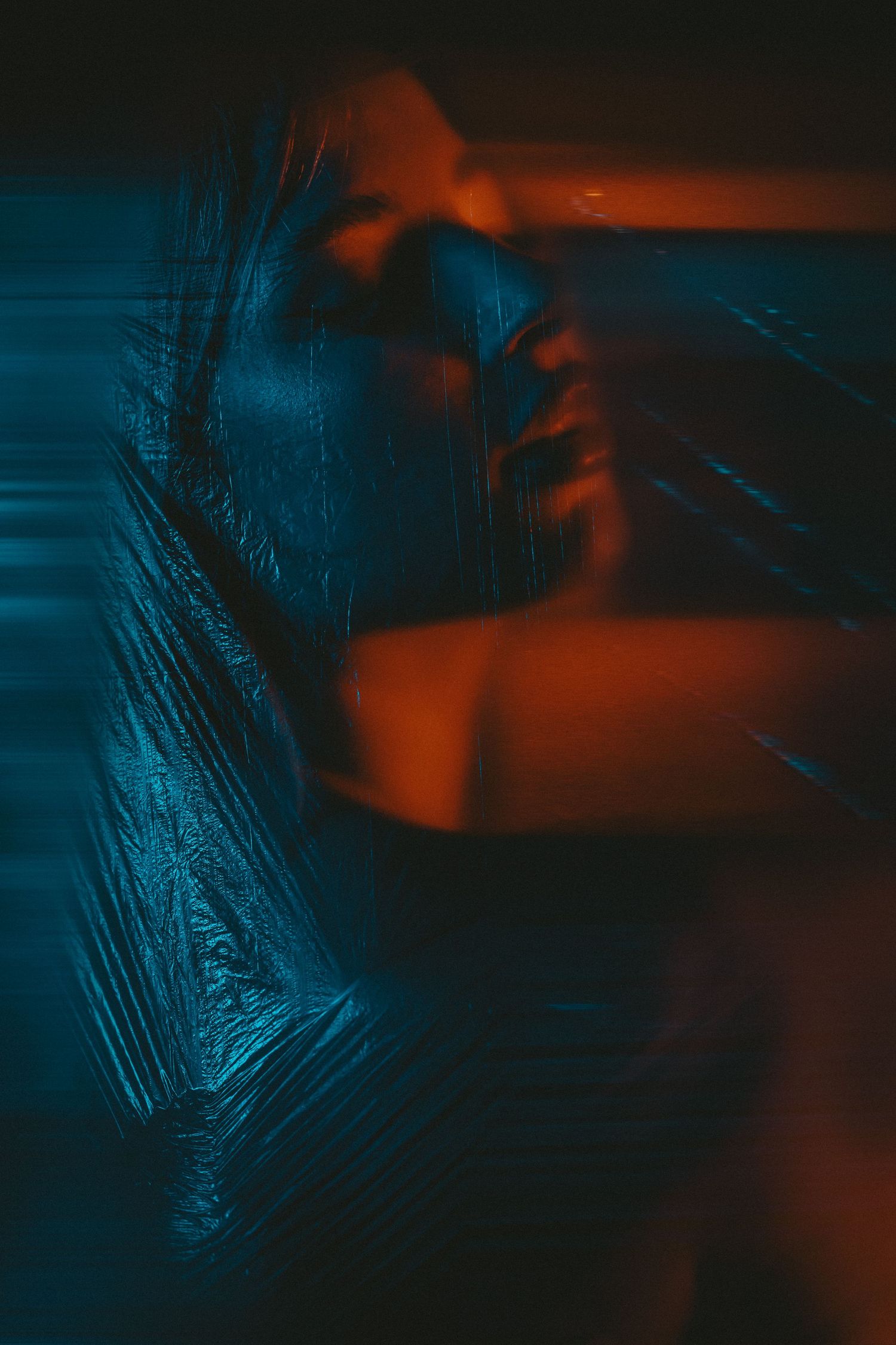 Artistic portrait of a woman wrapped in plastic film under dramatic blue and orange neon lighting.