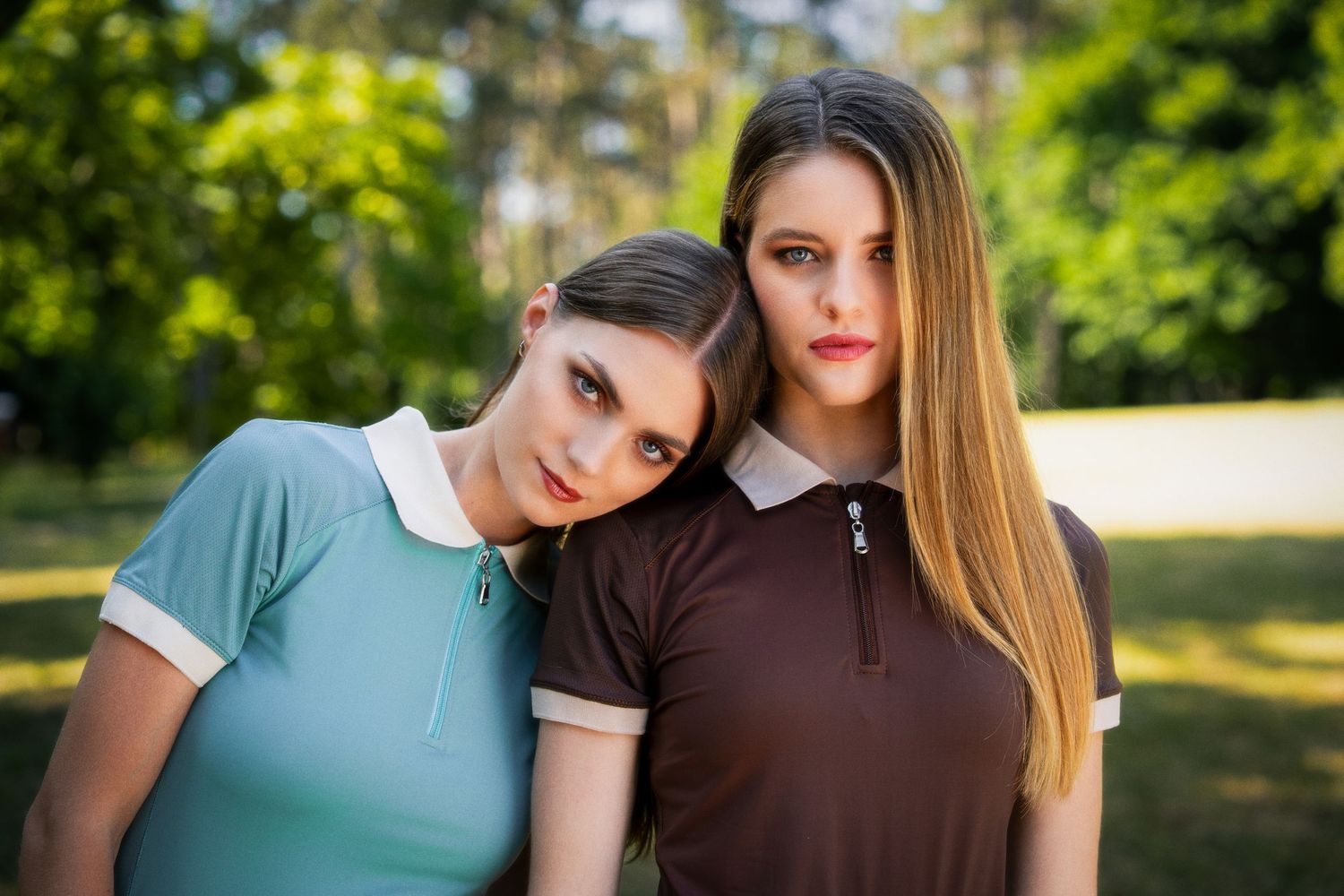 Two young women in polo shirts pose together outdoors with green trees in the background.