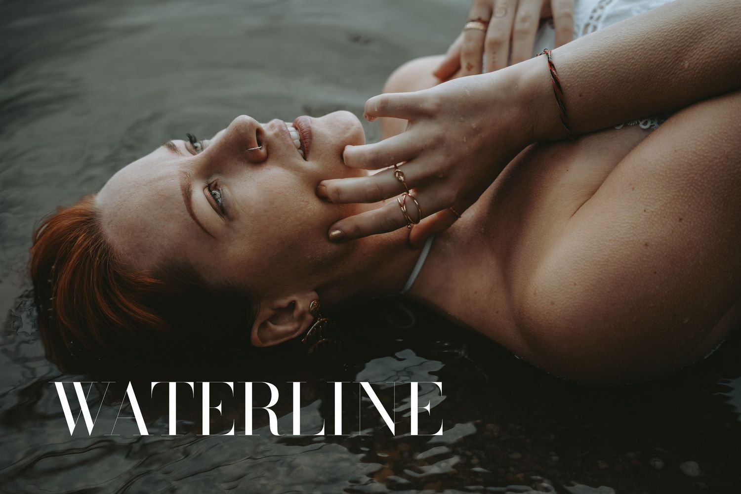 Woman with red hair floating in water wearing gold rings, with Waterline text overlay in elegant typography.