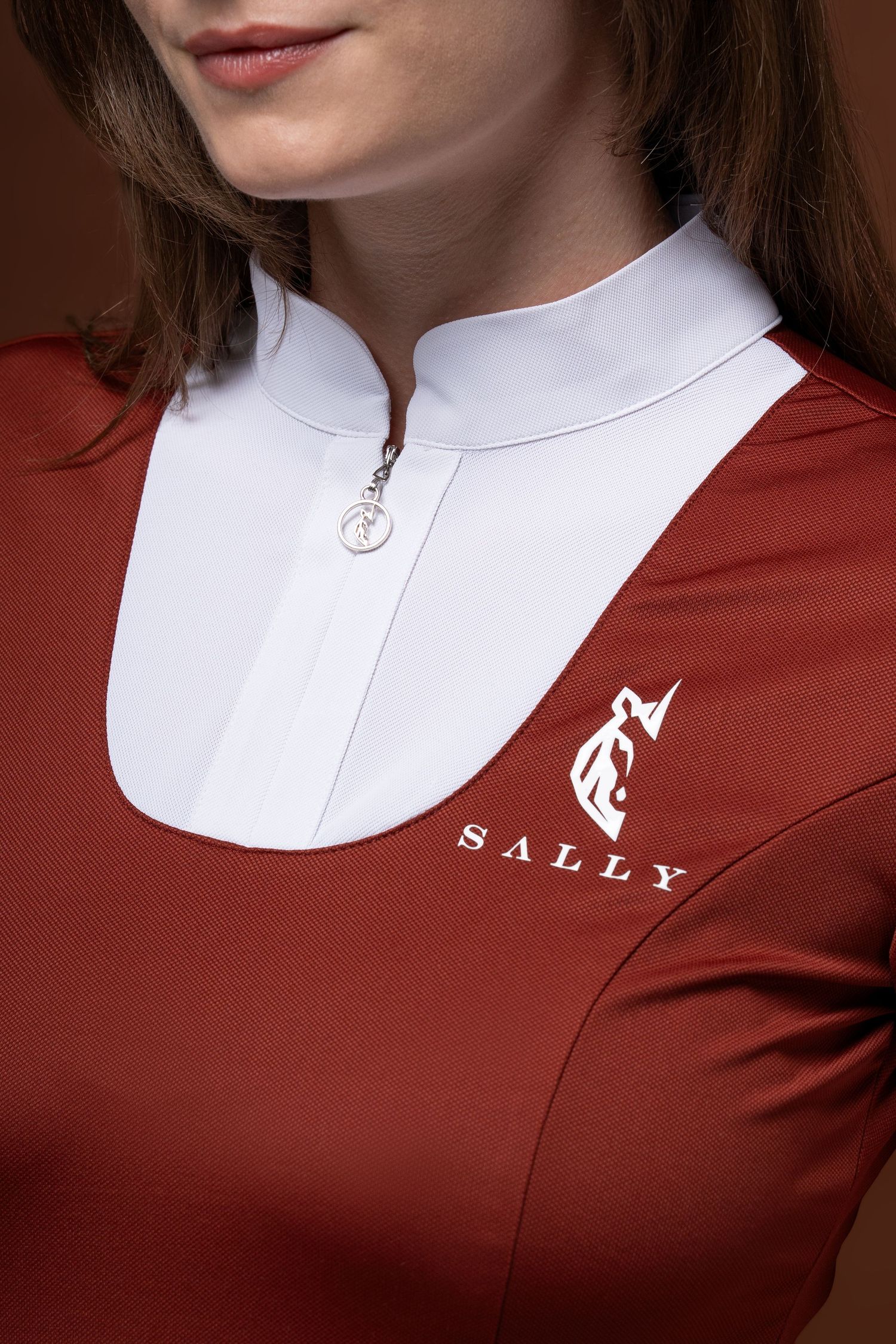 Detail shot of Sally logo on burgundy and white equestrian show shirt with decorative zipper pull.
