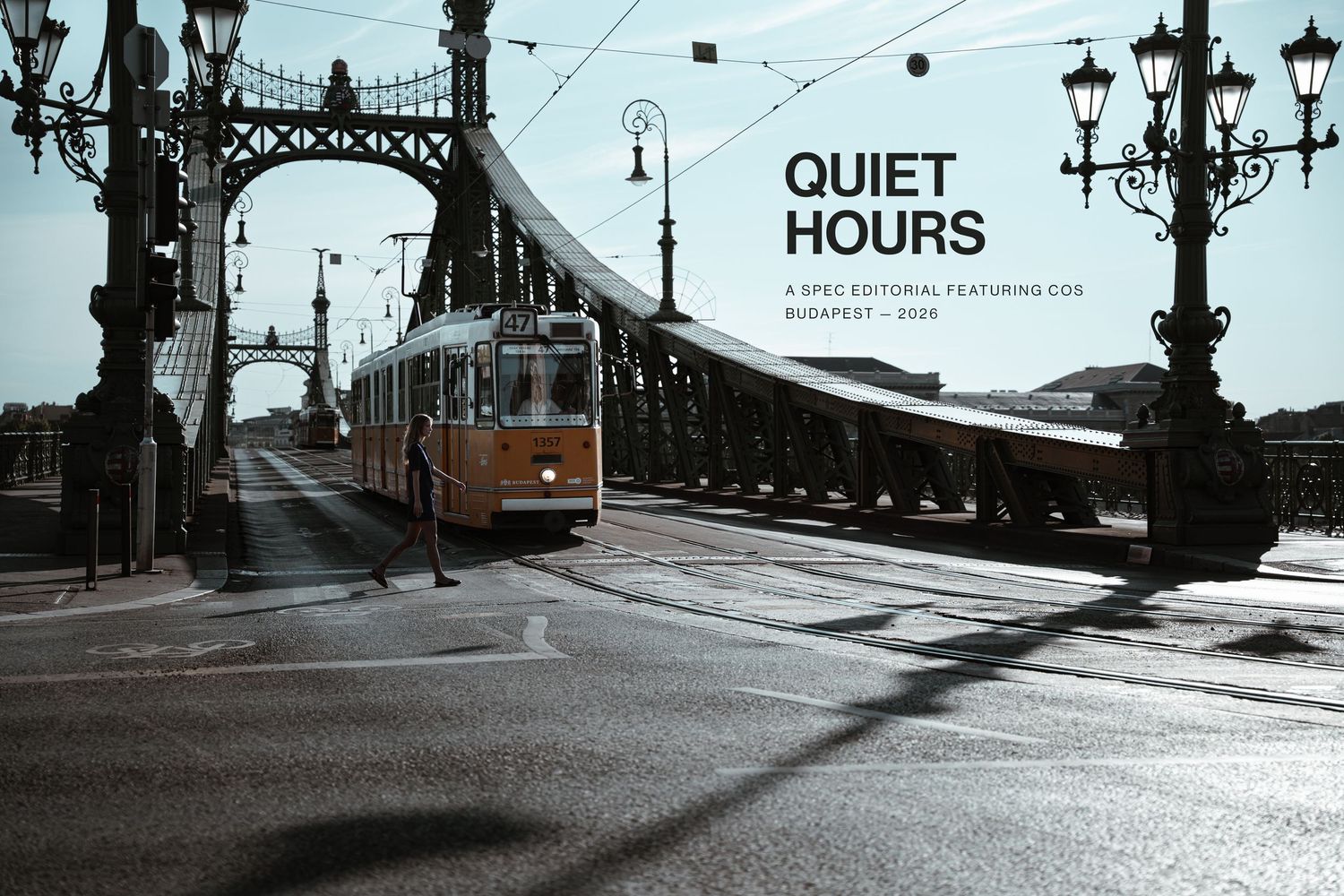 A vintage yellow tram crosses a historic bridge in Budapest during quiet hours, with ornate lamp posts lining the misty street.