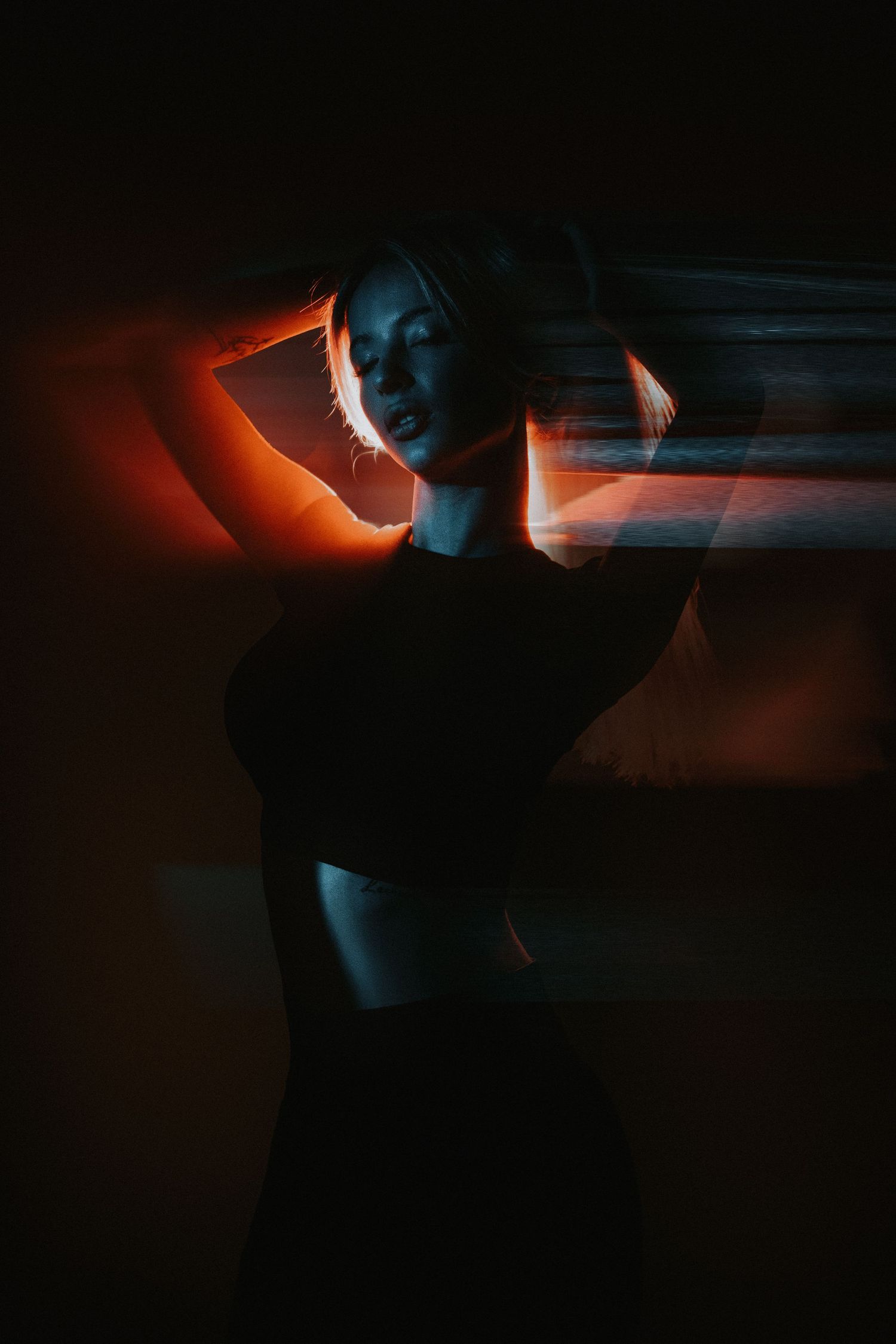 Woman in black crop top posing with motion blur effect under dramatic orange and blue neon lighting.