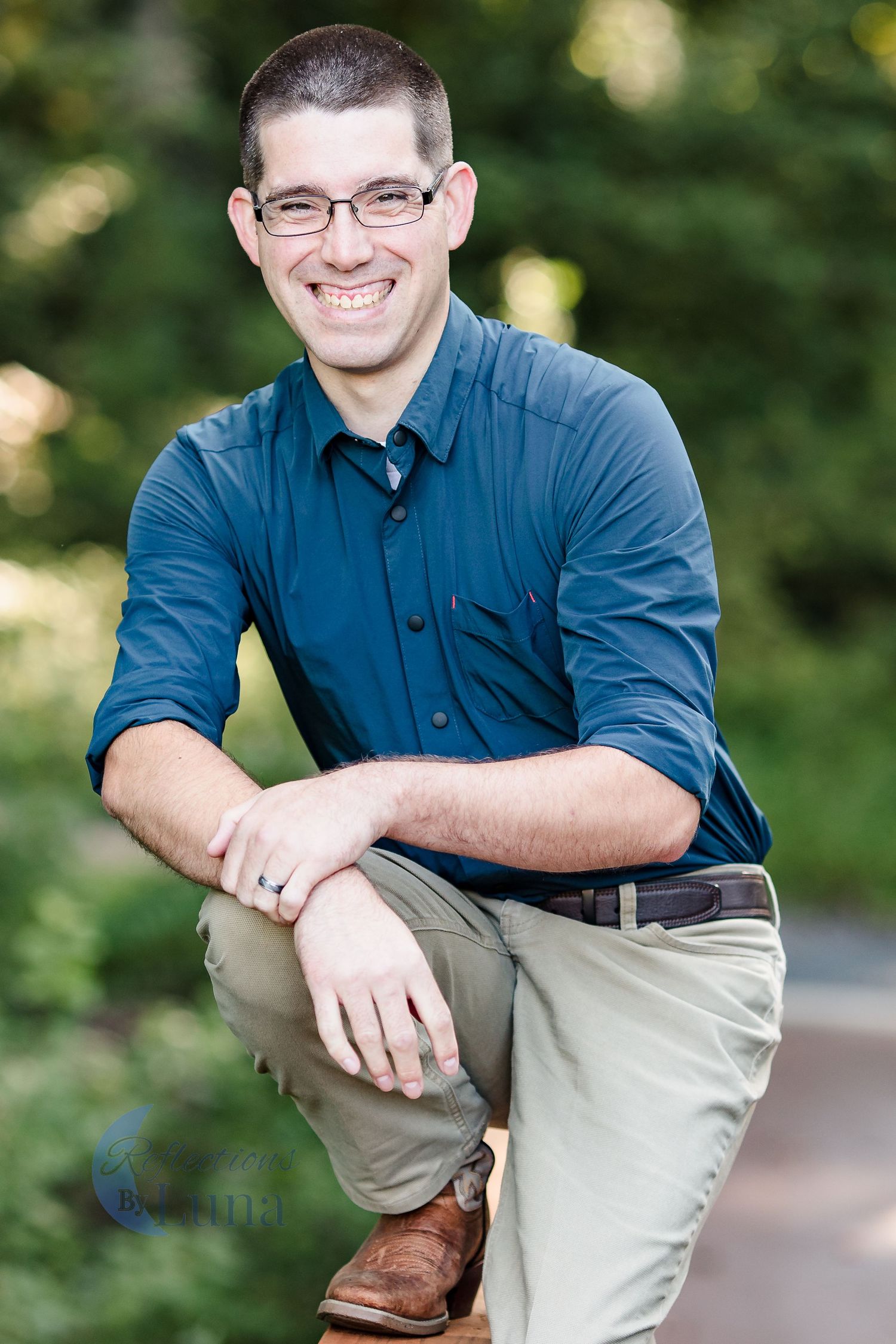 Crouching portrait on path — Casual outdoor branding portrait of man in navy shirt and glasses crouching on a path and smiling warmly.
