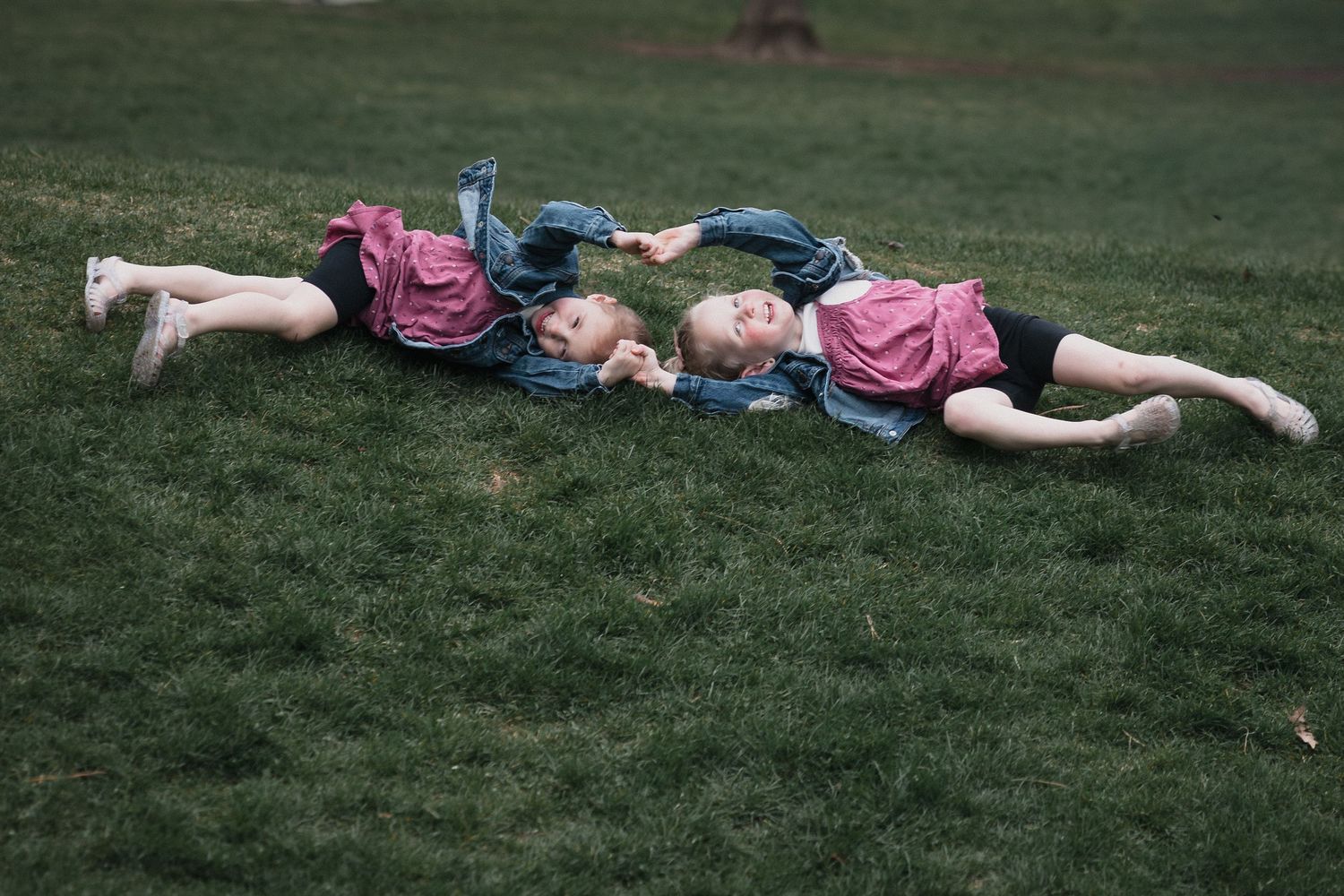 Two girls in pink on grass — Two young girls in matching pink shirts lying on green grass, smiling together.