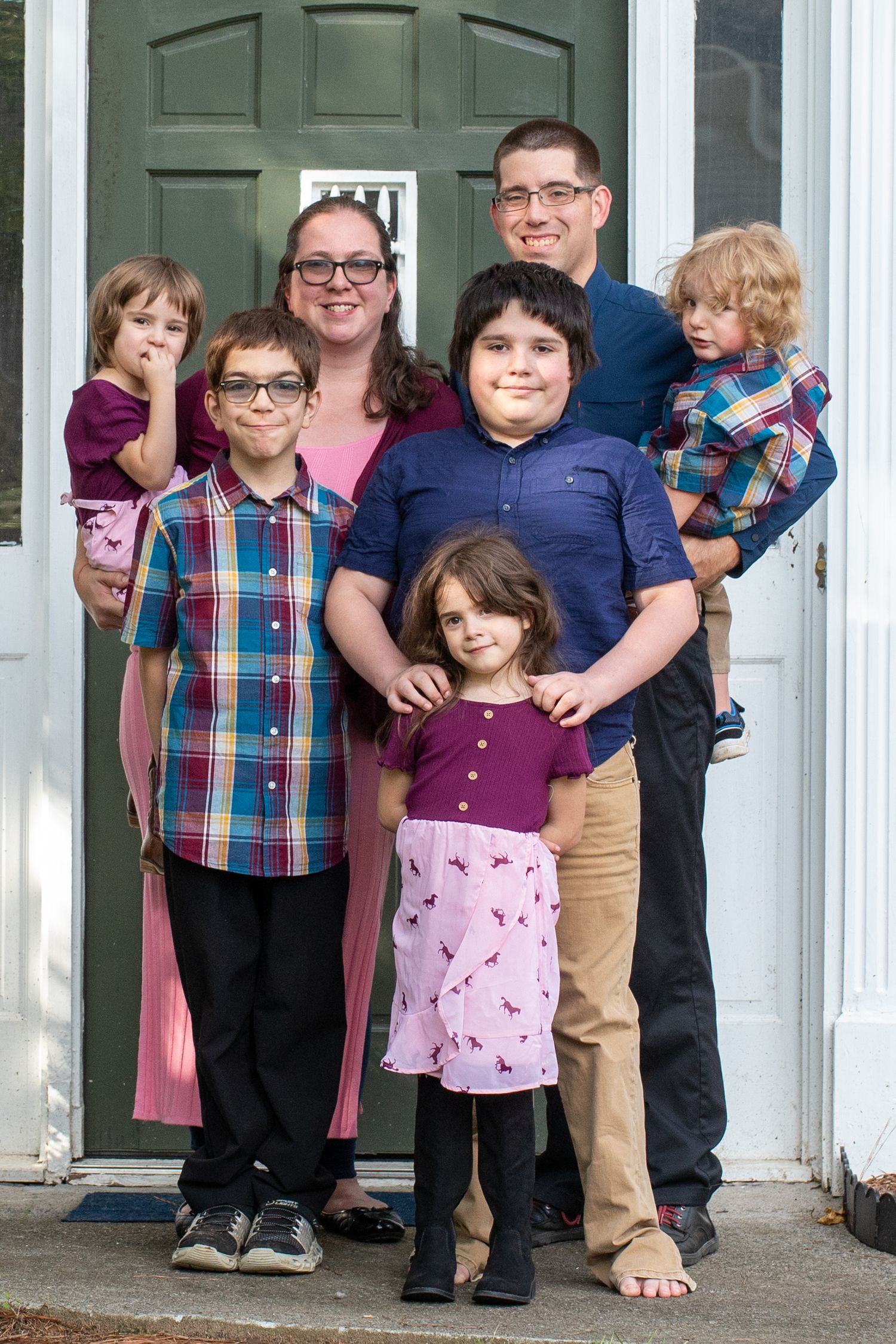 Family of seven doorway — Smiling family of seven posing together at their front door in coordinating purple and blue outfits.