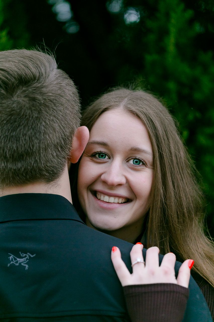 Woman hugging man from behind — Smiling woman with green eyes hugging her partner from behind outdoors, resting her head on his shoulder.