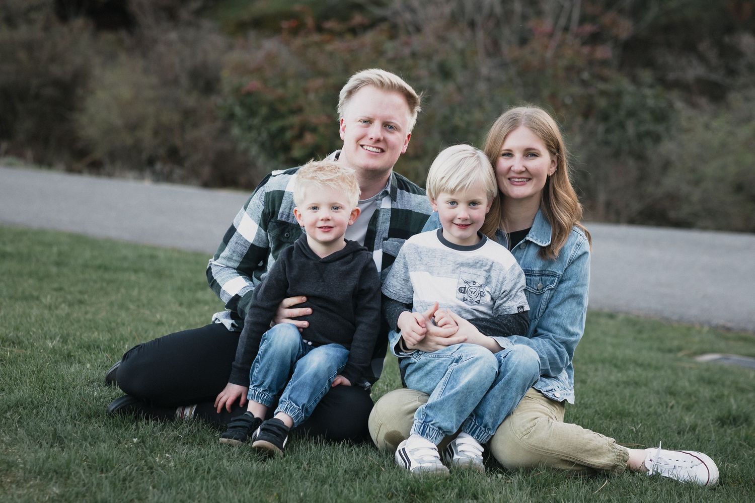 Family of four autumn grass — Happy family of four sitting on green grass in a park during spring, smiling together in natural light.