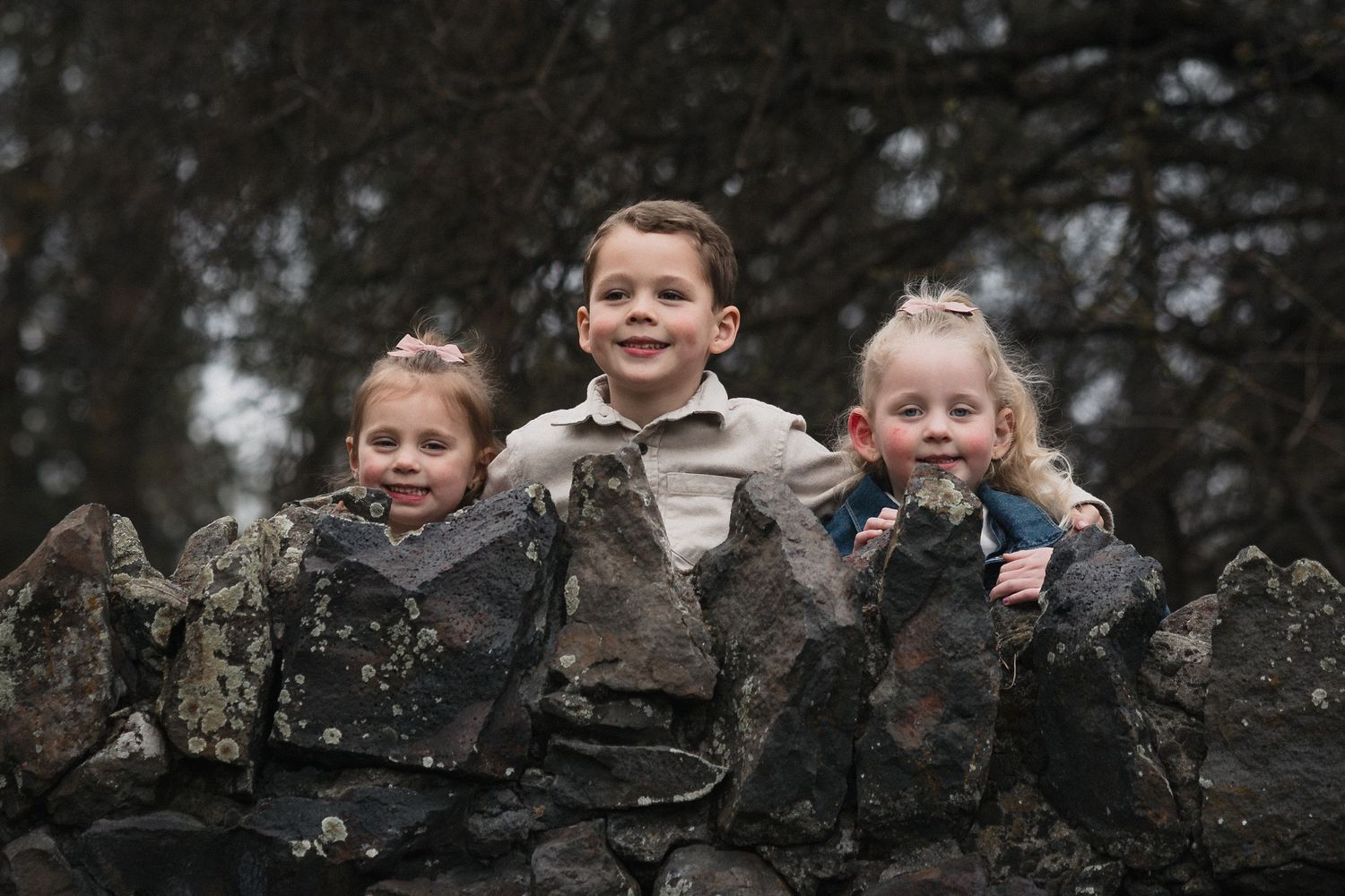 Kids peeking over stone wall — Three young children peeking over a rustic stone wall during an outdoor session.