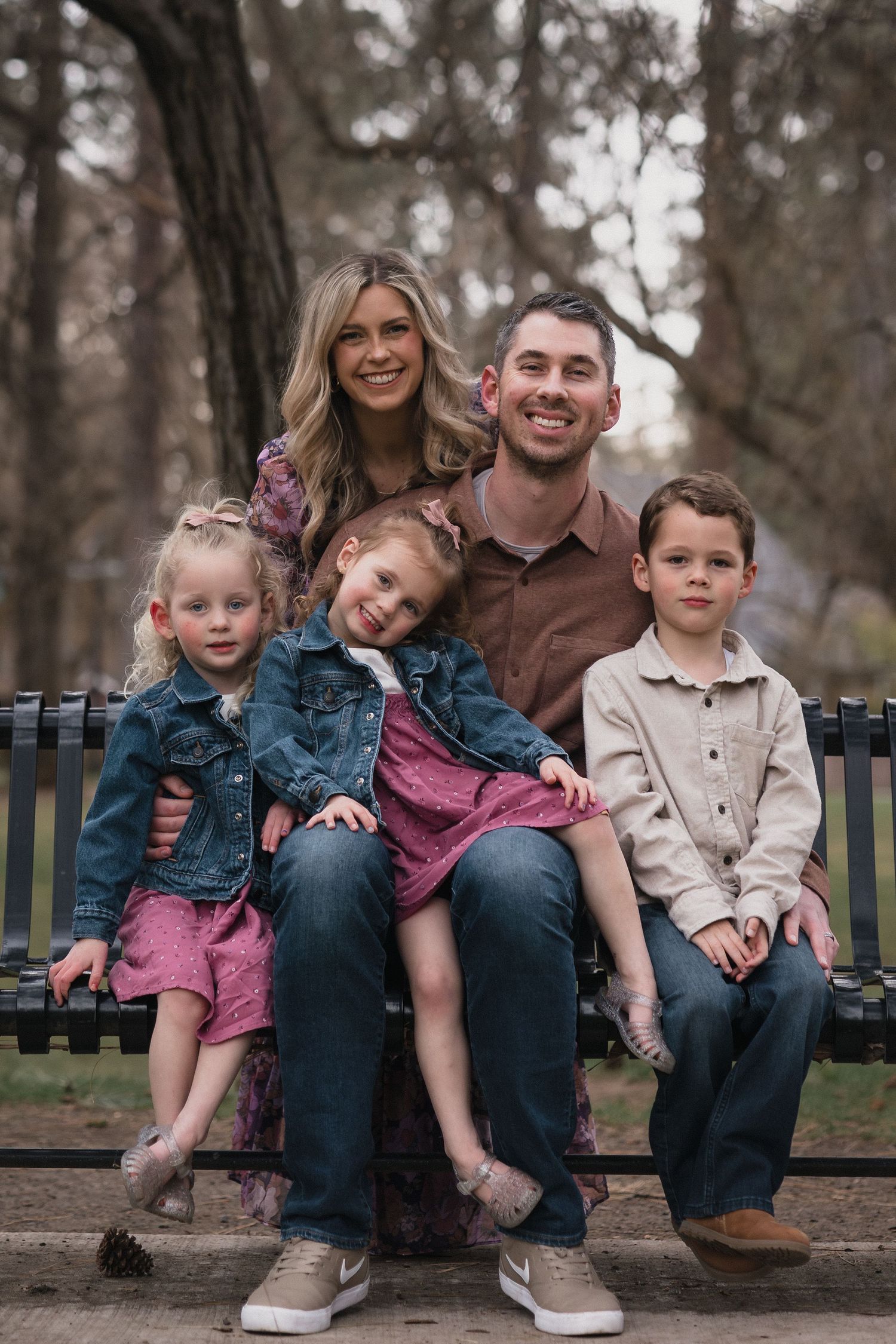 Family of five on bench — Happy family of five posing together on a park bench surrounded by trees.