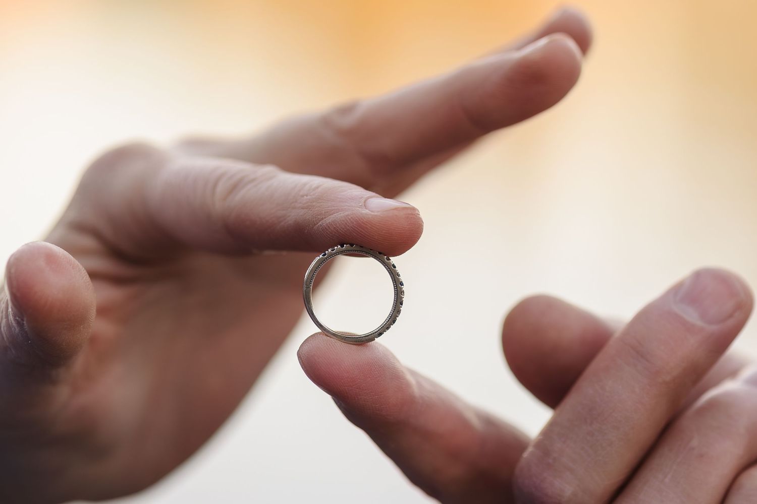 Hands holding silver ring — Close‑up detail of hands holding a delicate silver ring with textured band in soft natural light.