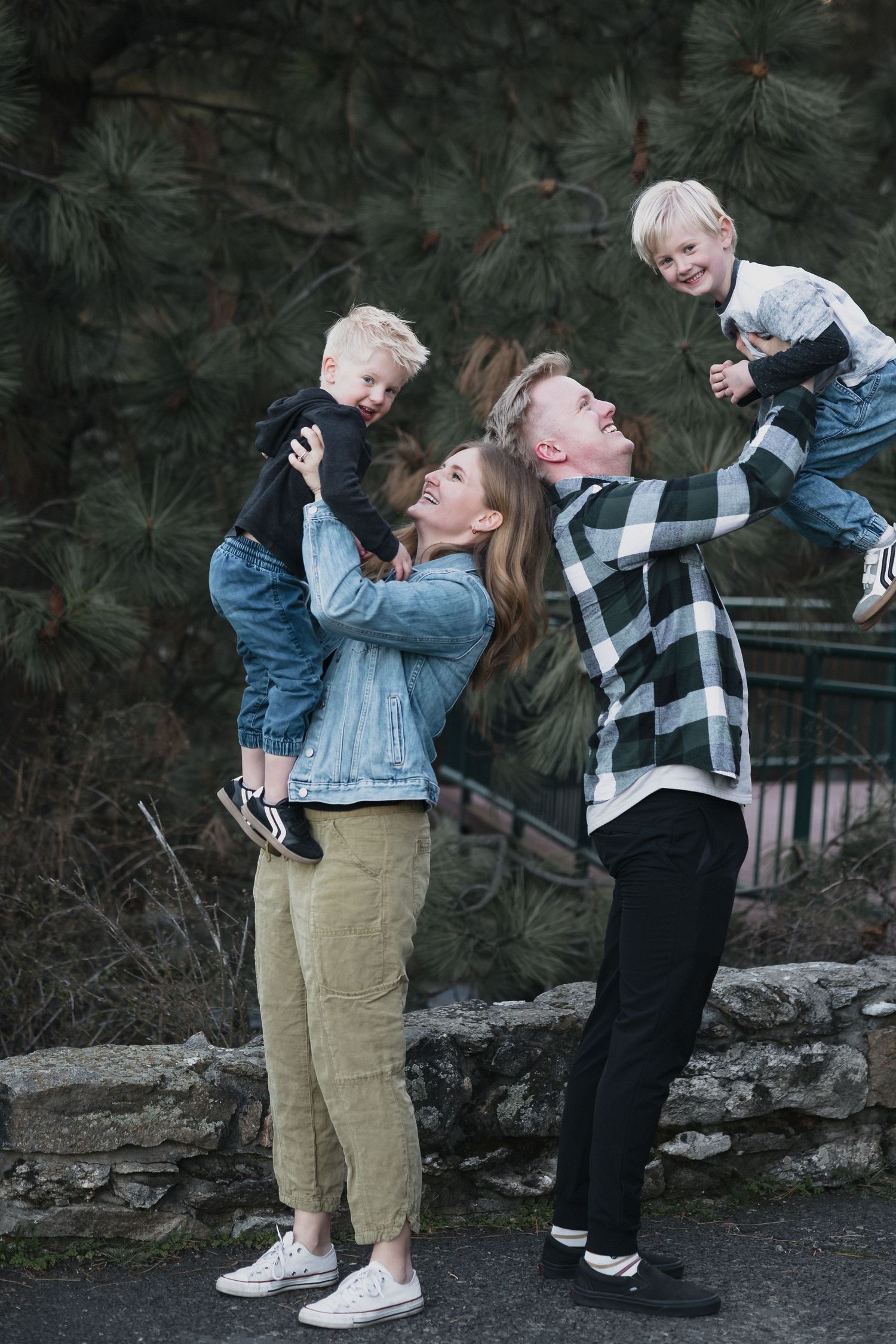 Parents lifting toddlers — Playful family moment with parents lifting two laughing blonde toddlers near a stone wall outdoors.