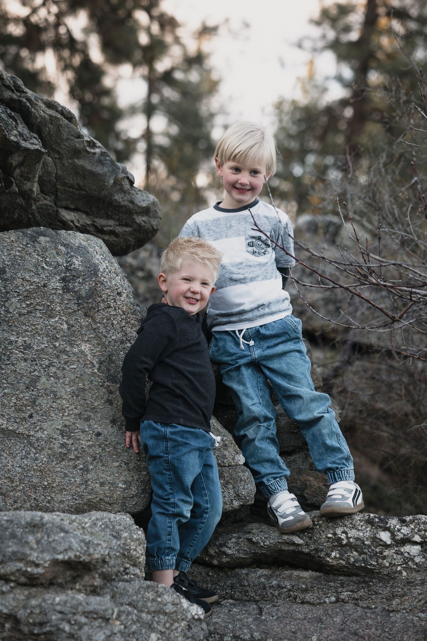 Two blonde brothers forest rocks — Outdoor portrait of two young blonde brothers smiling and posing together on rocky boulders.
