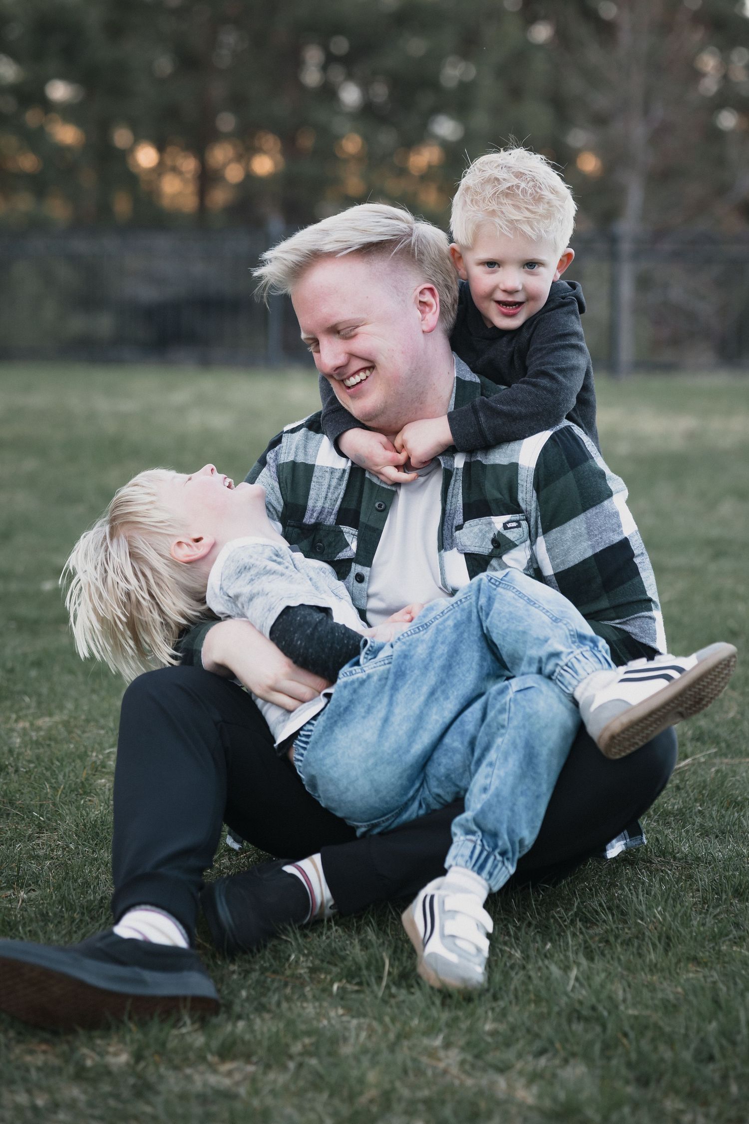 Boys climbing on dad — Father laughing while his two young blonde sons playfully climb on him during an outdoor session.